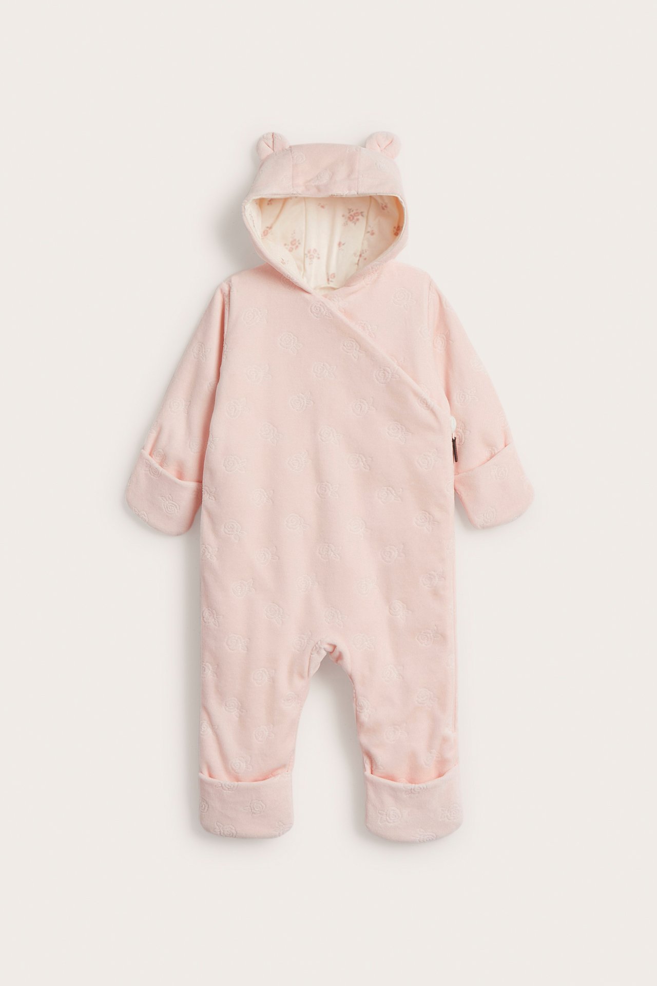 Frontvy: rosa velouroverall för baby med präglat mönster, huva med öron och vikbara muddar.