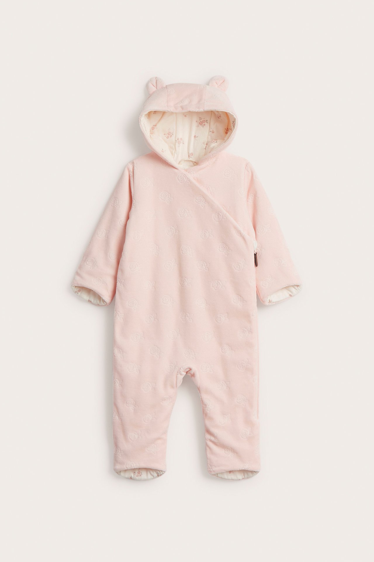 Frontvy: Babyrosa velouroverall med präglat mönster, öronhuva, diagonal dragkedja och blommigt foder.