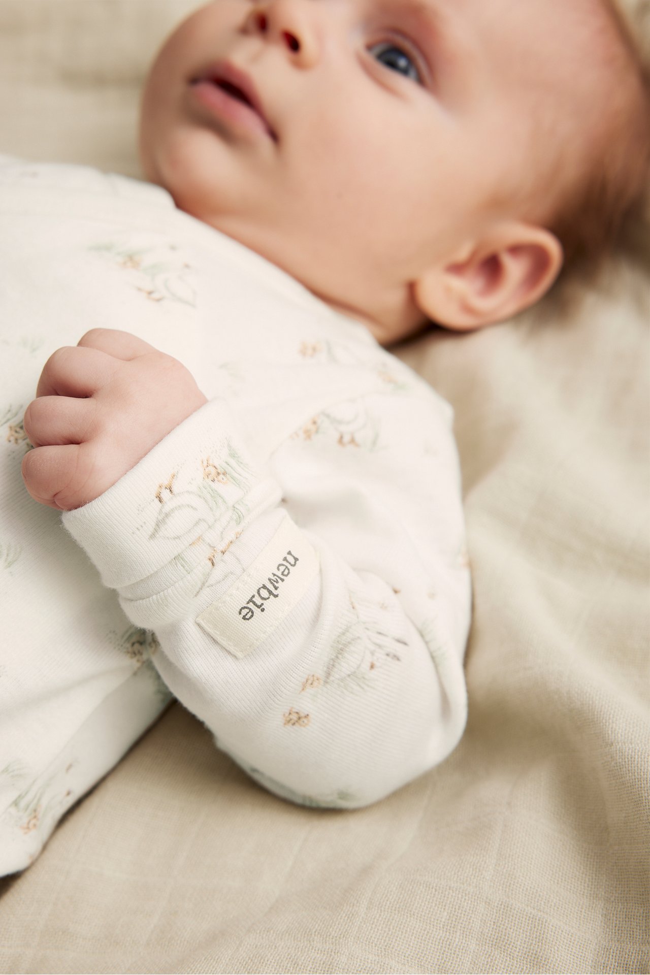 Närbild på baby i offwhite ribbad omlottbody i ekologisk bomull med diskret mönster.