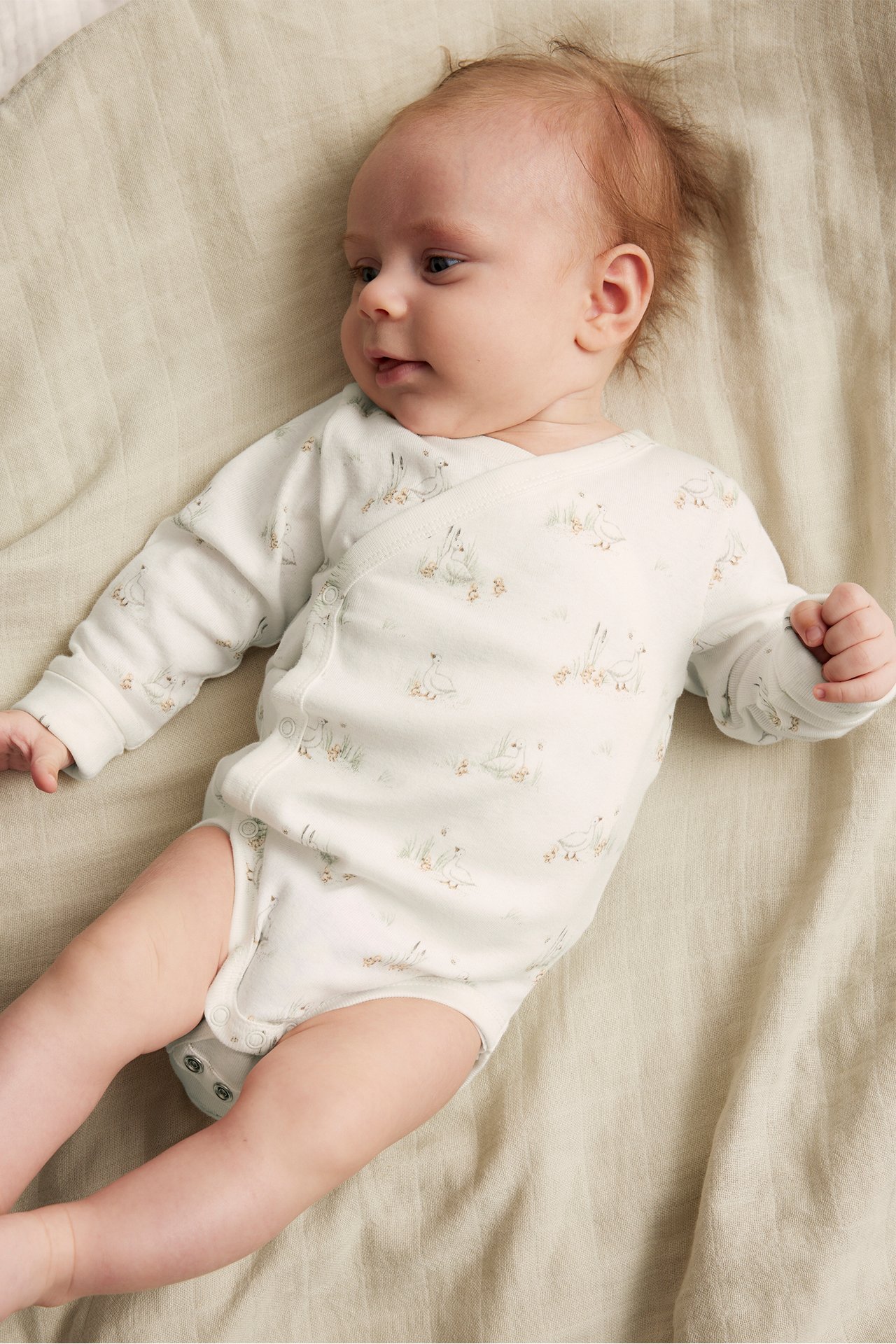 Uppifrån: baby i offwhite ribbad omlottbody i ekologisk bomull med ankprint och tryckknappar.