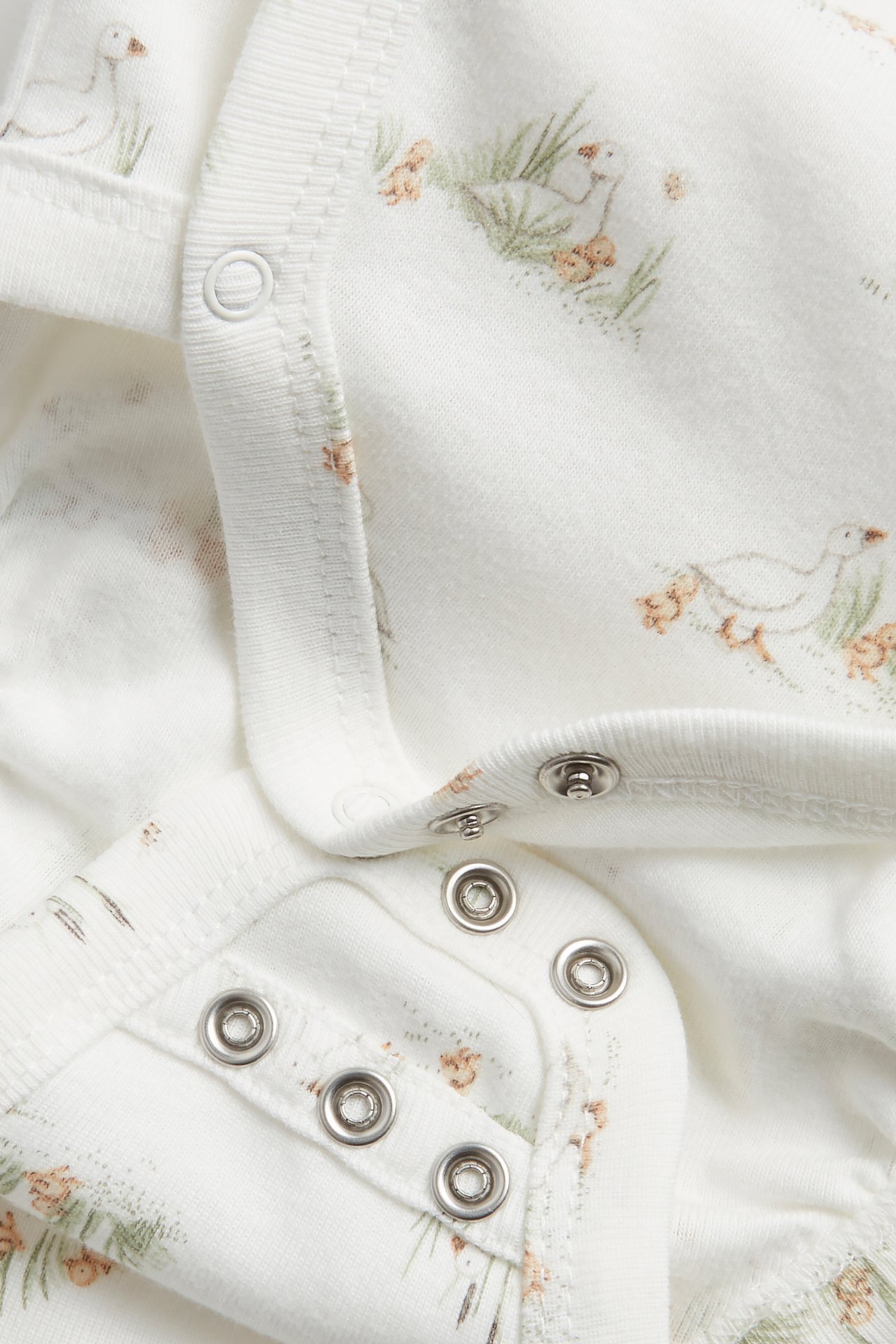 Närbild av en offwhite ribbad bomullsbody med omlottknäppning, ankprint och tryckknappar.