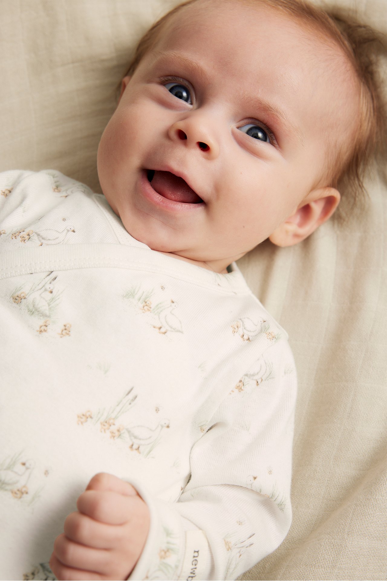 Närbild på en leende baby i en offwhite ribbad omlottbody med ank-mönster.