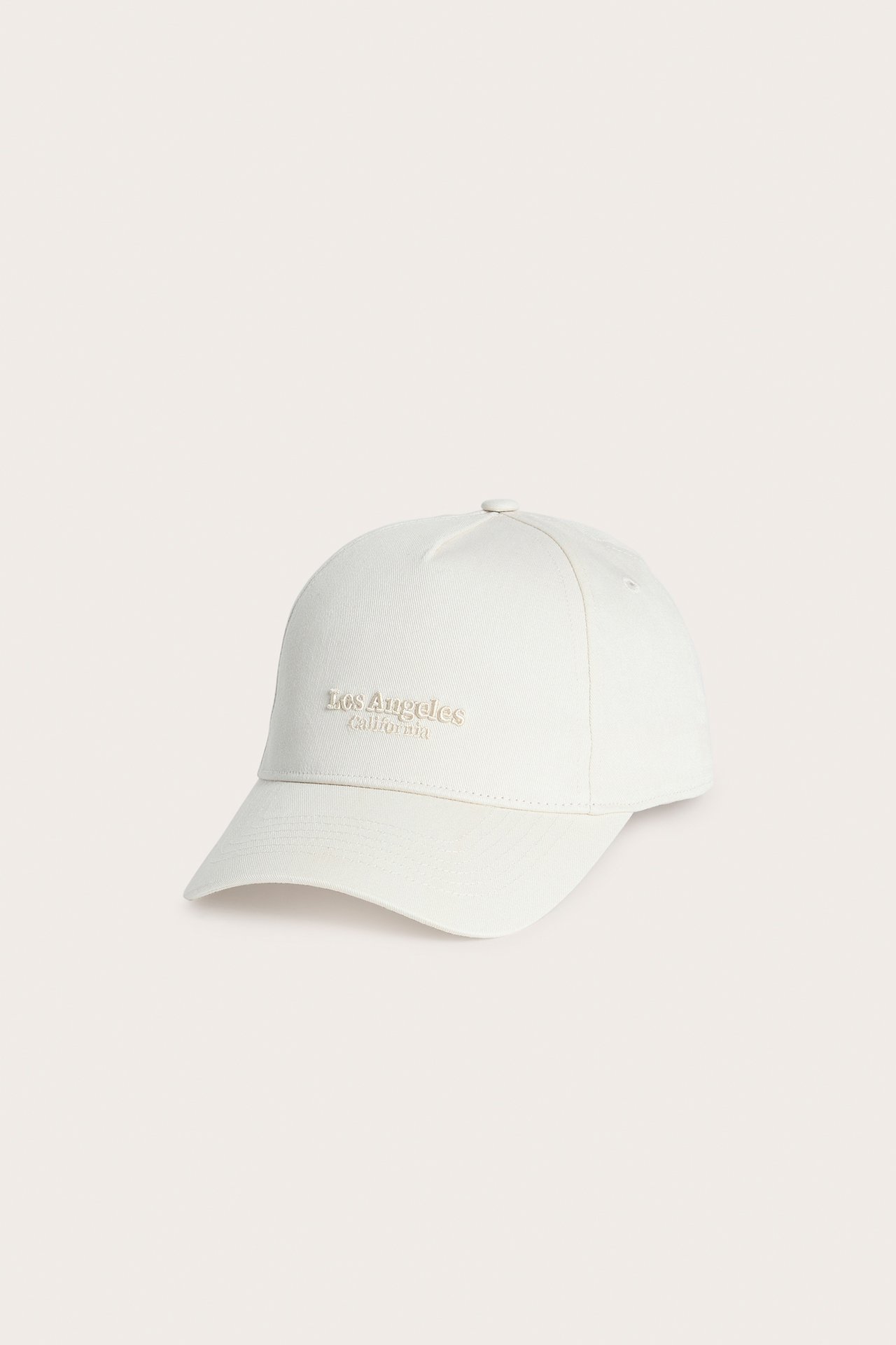 Frontvy av en ljusbeige keps med "Los Angeles California" broderat framtill.