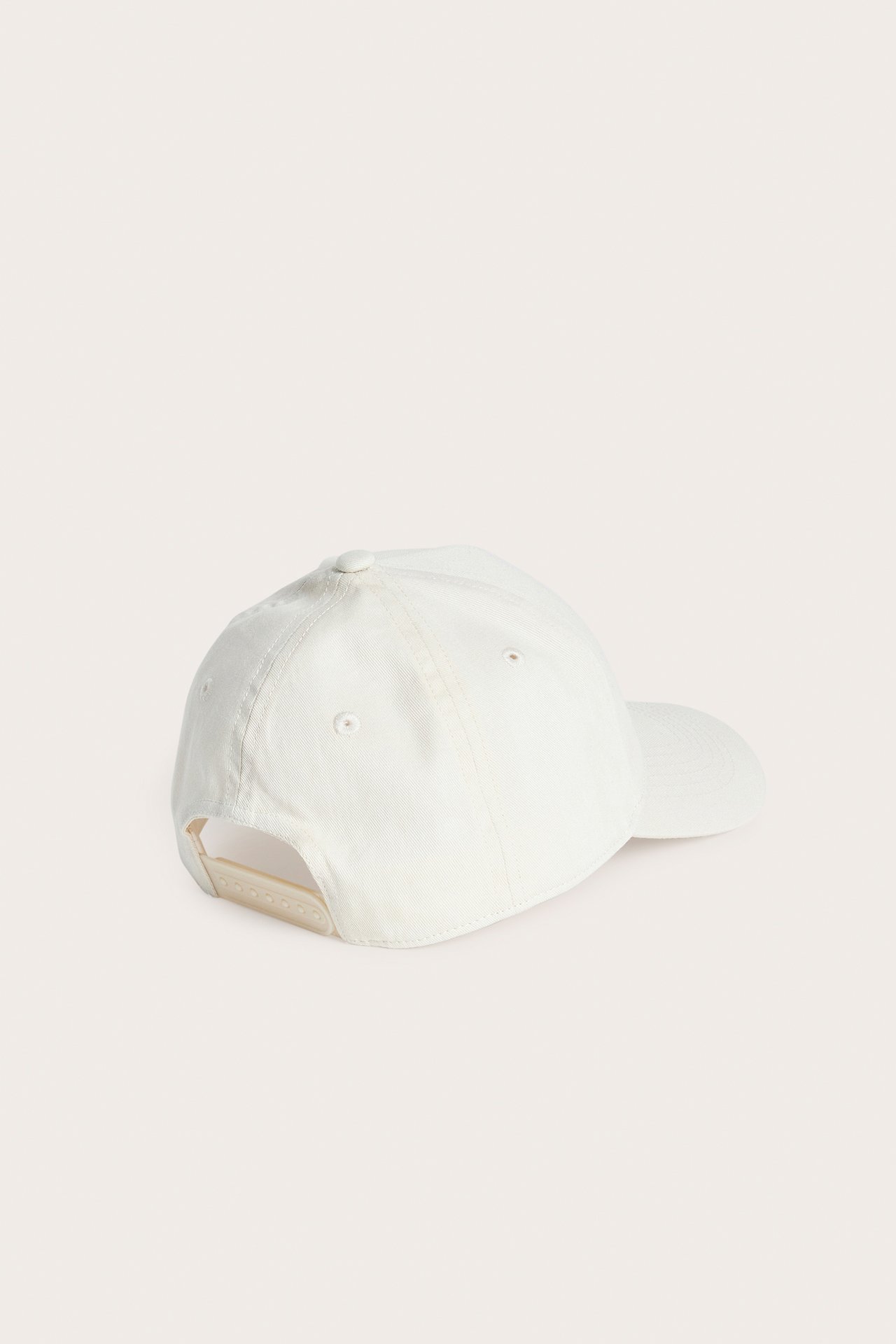 Bakifrån, en ljusbeige keps med justerbar remstängning.