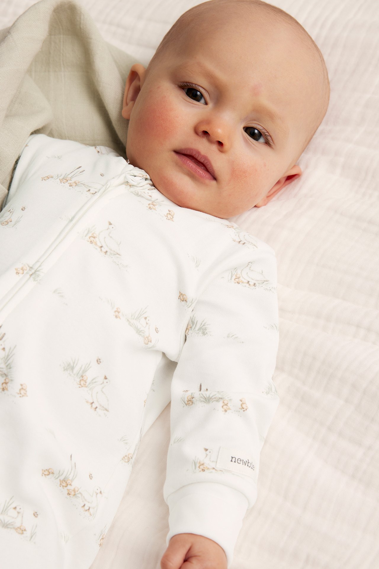Edestäpäin, vauva yllään luonnonvalkoinen puuvillapyjama ankka-kuviolla ja vetoketjulla edessä.