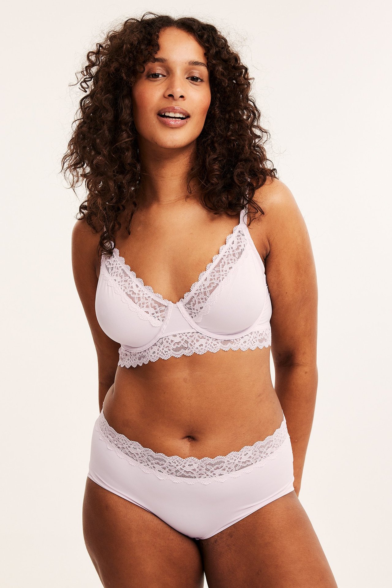 Frontvy av en kvinna i en ljusrosa ovadderad bh med spetsdetaljer och matchande trosor.