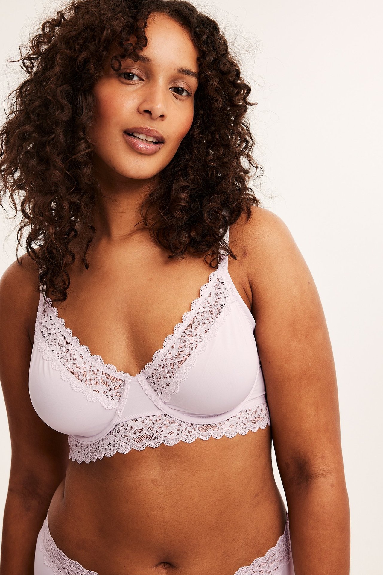 Framifrån, kvinna i ljusrosa ovadderad spets-bh och matchande trosa.