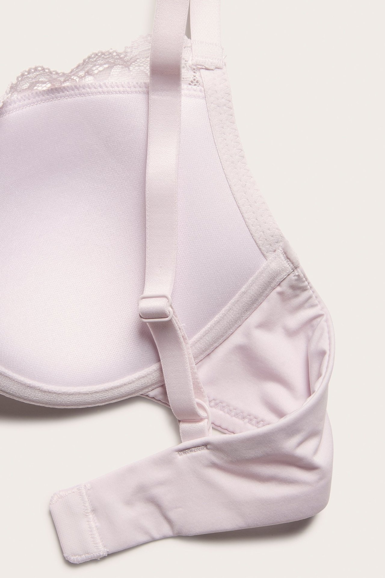 Zbliżenie jasnoróżowego, usztywnianego biustonosza z fiszbinami, koronkowym wykończeniem i regulowanym ramiączkiem.
