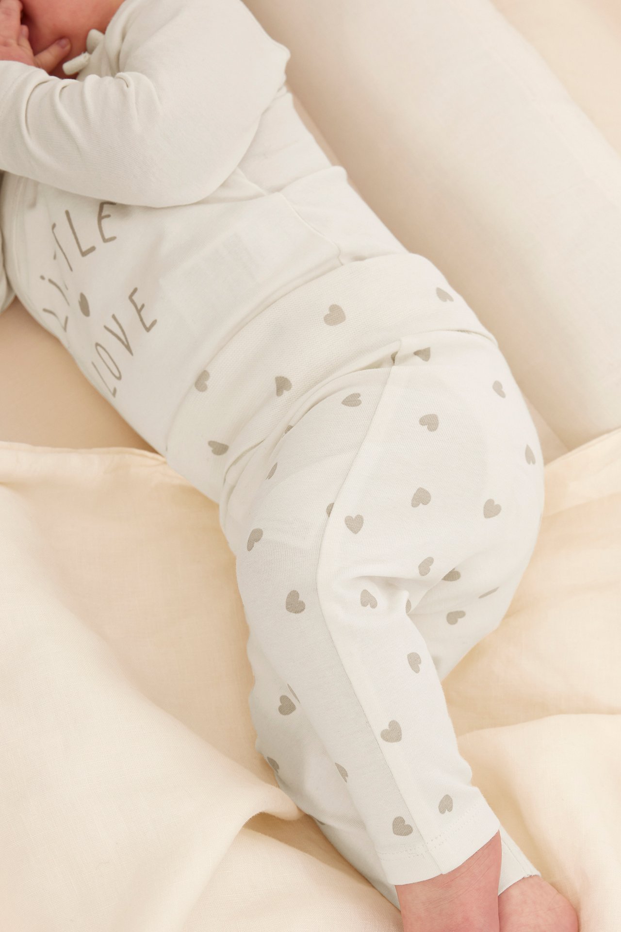 Ovanifrån: Baby i offwhite bodysuit med texten 'LITTLE LOVE' och hjärtmönstrade byxor.