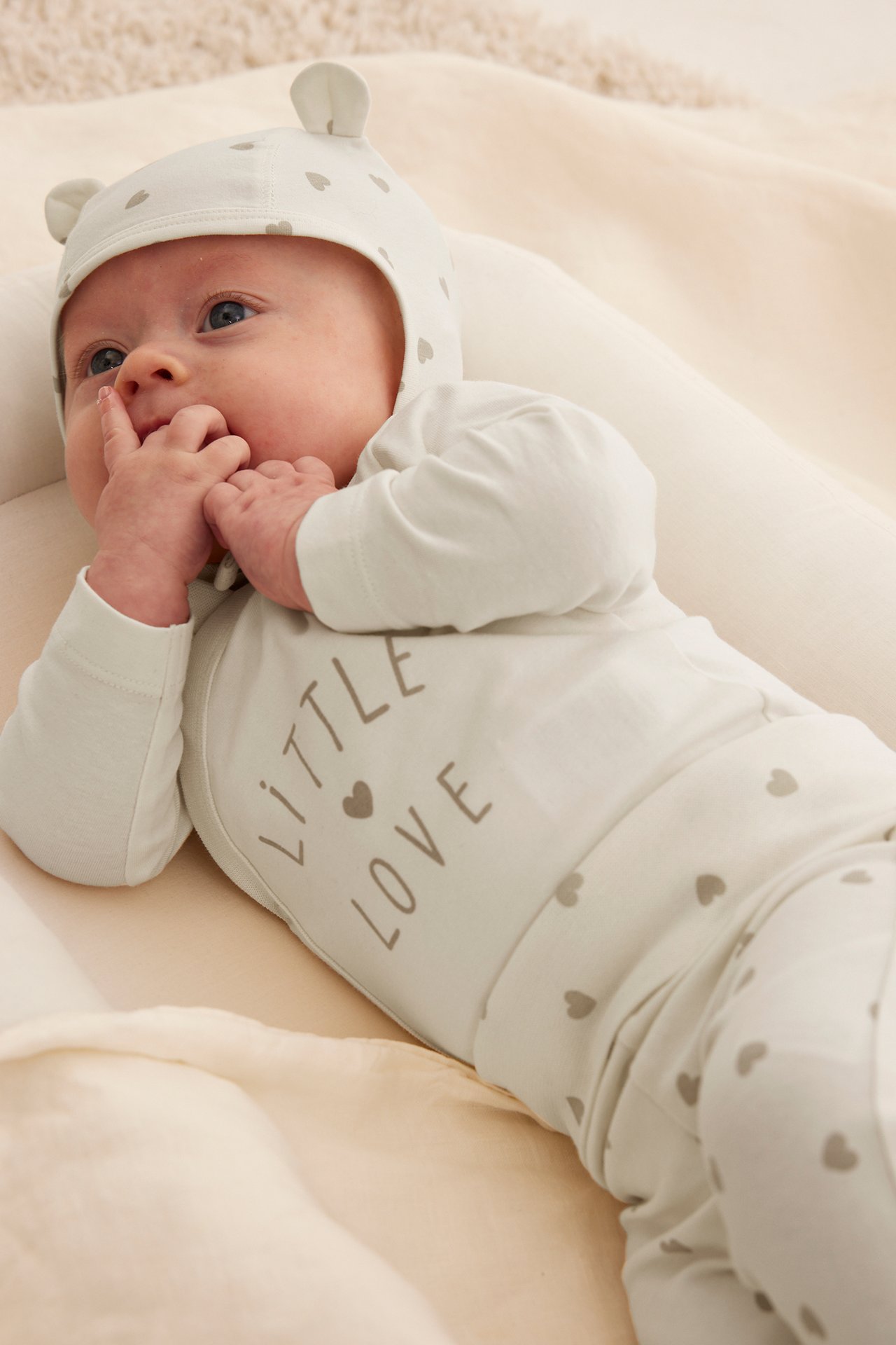 Närbild på baby i offwhite mönstrad body med texten 'LITTLE LOVE' och matchande mössa med öron.