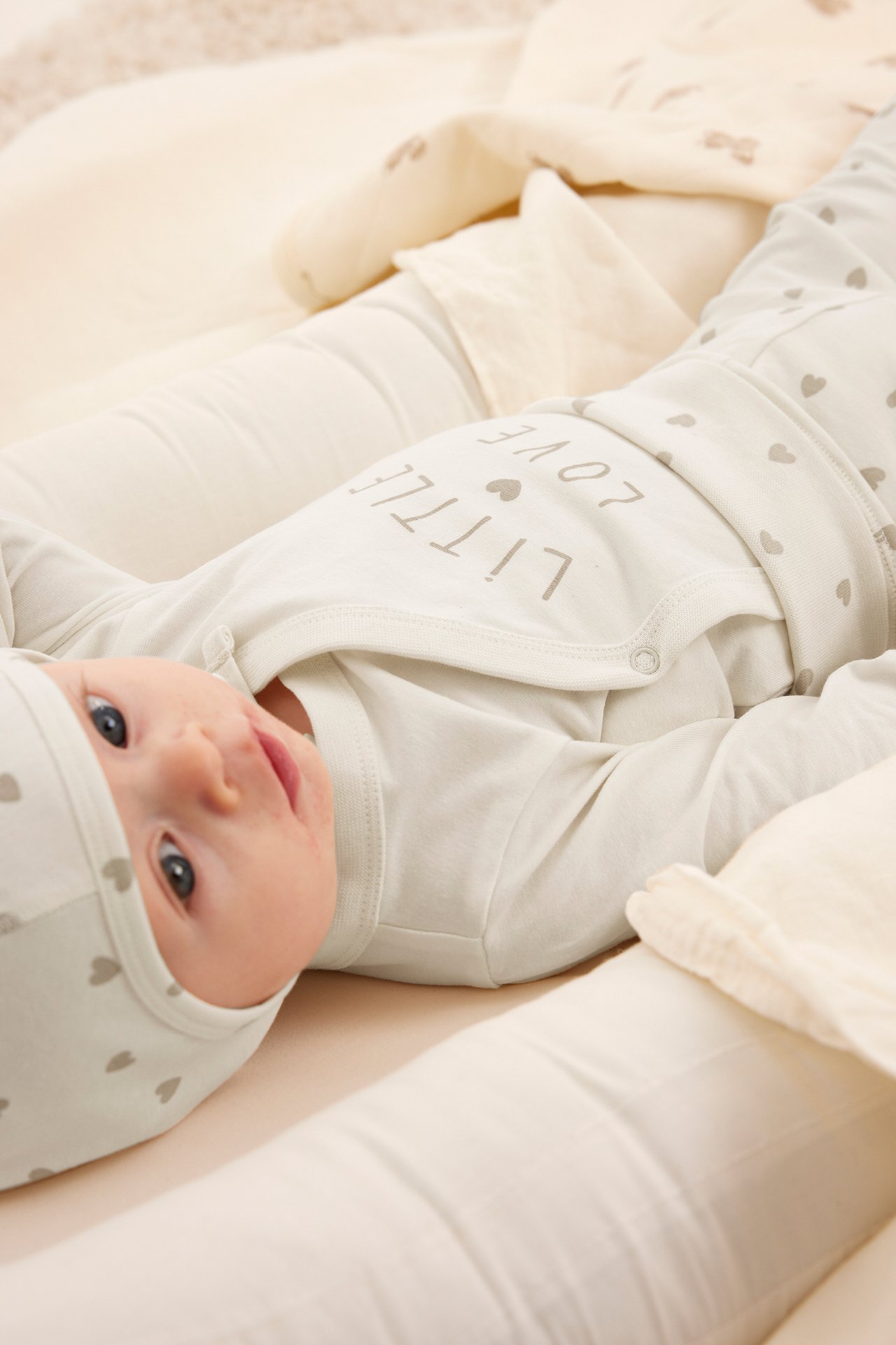 Uppifrån: baby i offwhite 'LITTLE LOVE' body, hjärtmönstrade byxor och mössa.