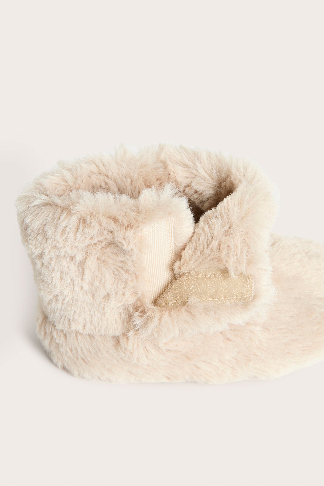 Närbild sidovy av en beige pile-tossa för baby med dold kardborreknäppning.