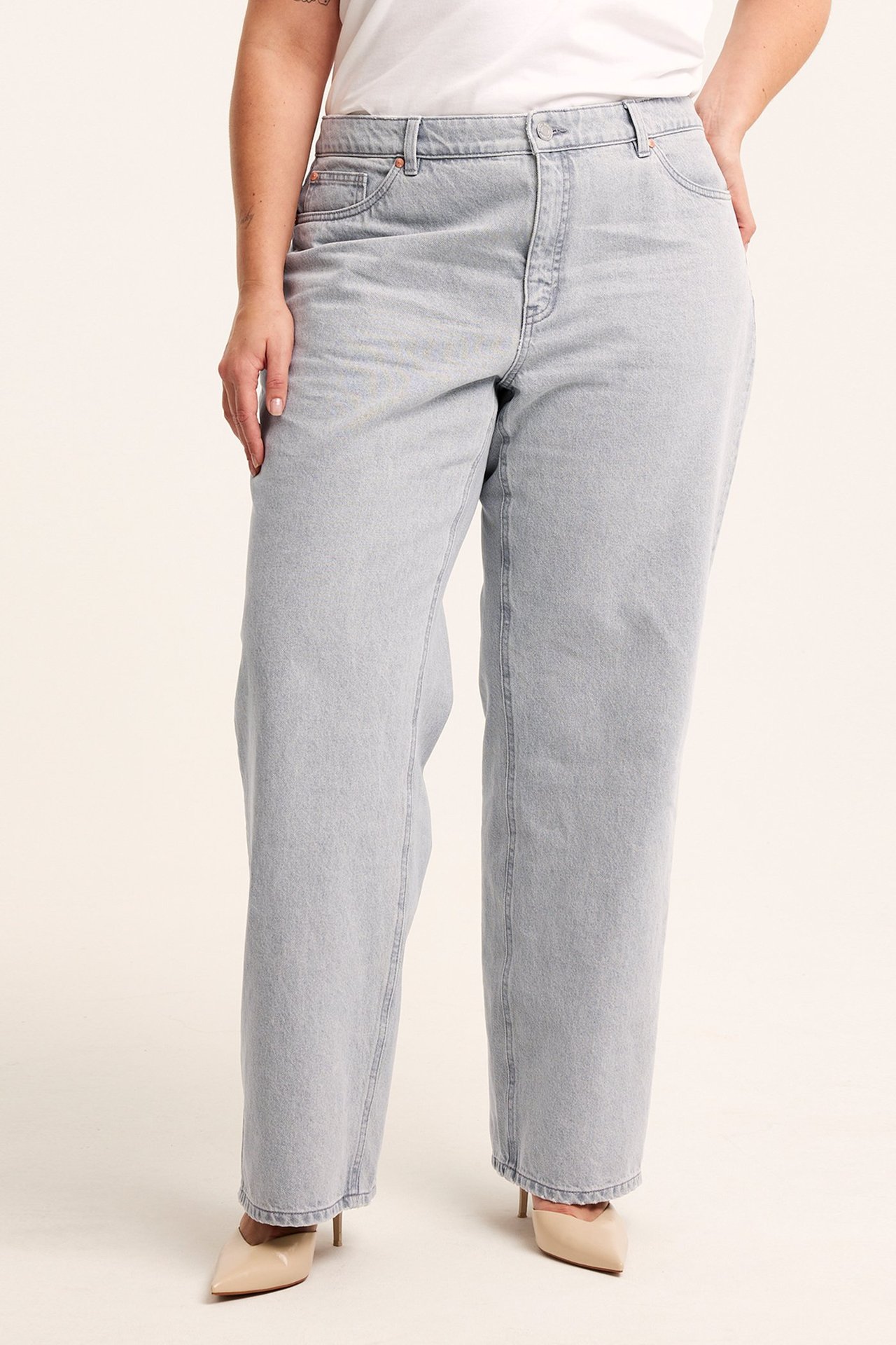 Frontbilde av kvinne i lysegrå, høye, vide bomullsjeans, hvit t-skjorte og beige høyhælte sko.