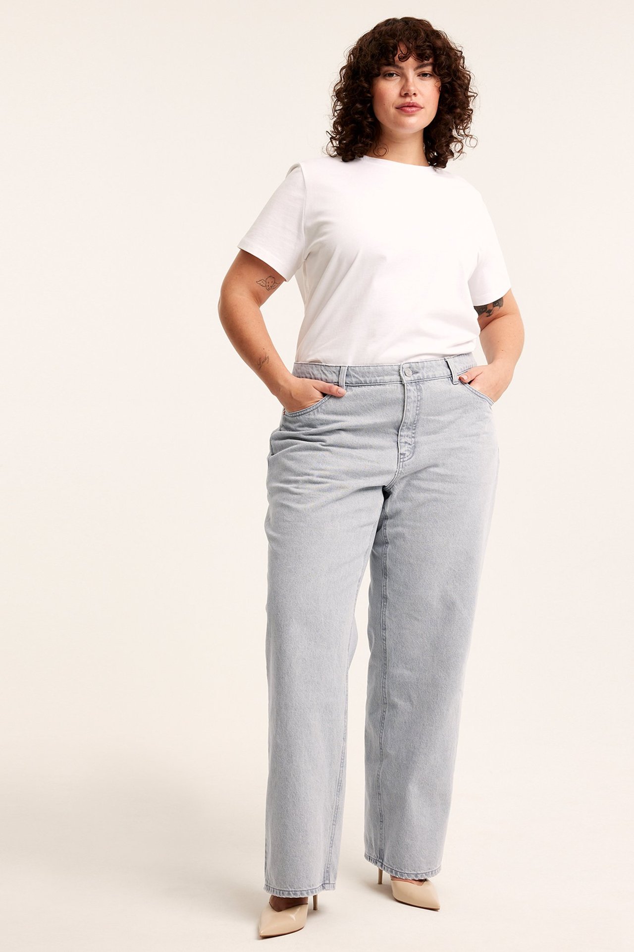 Forfra: kvinne i lysegrå vide jeans med høyt liv, hvit t-skjorte og beige pumps.