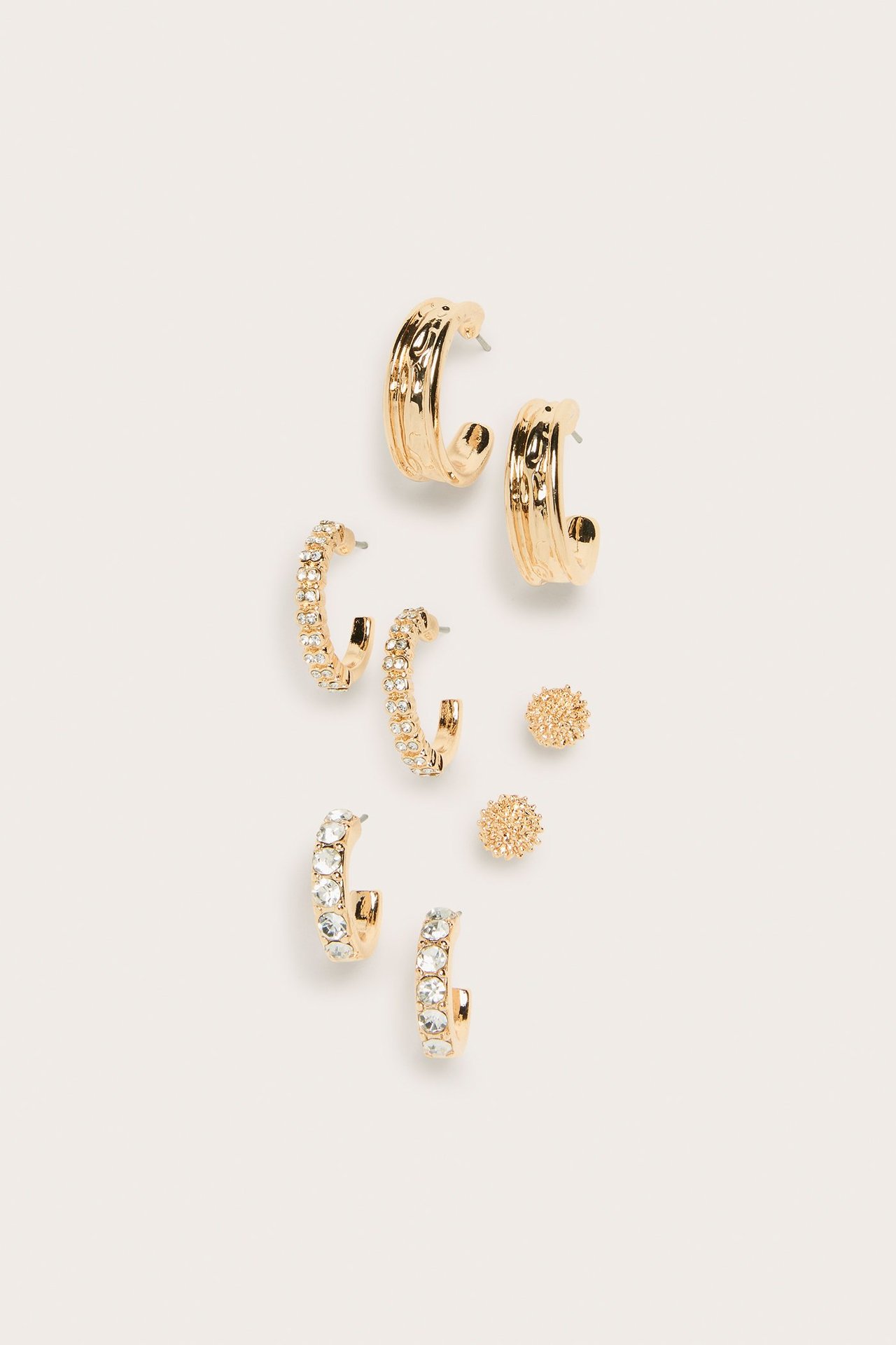 Widok z góry na 4-pak złotych kolczyków, w tym koła z przezroczystymi kamieniami i teksturowane sztyfty.