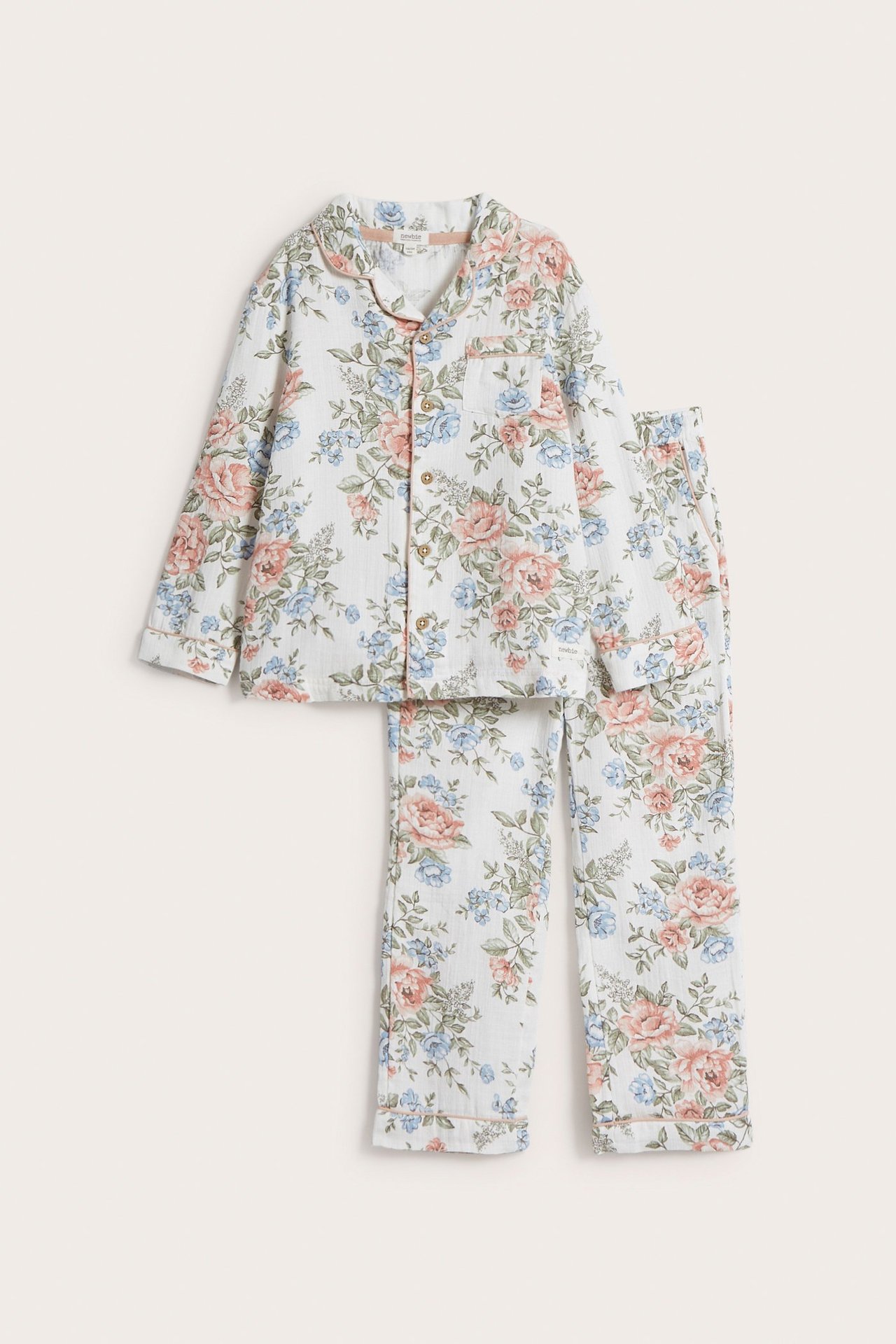 Edestä: Luonnonvalkoinen puuvillainen kukkakuvioinen pyjamassetti, jossa napitettu paita ja kiristysnyörilliset housut.