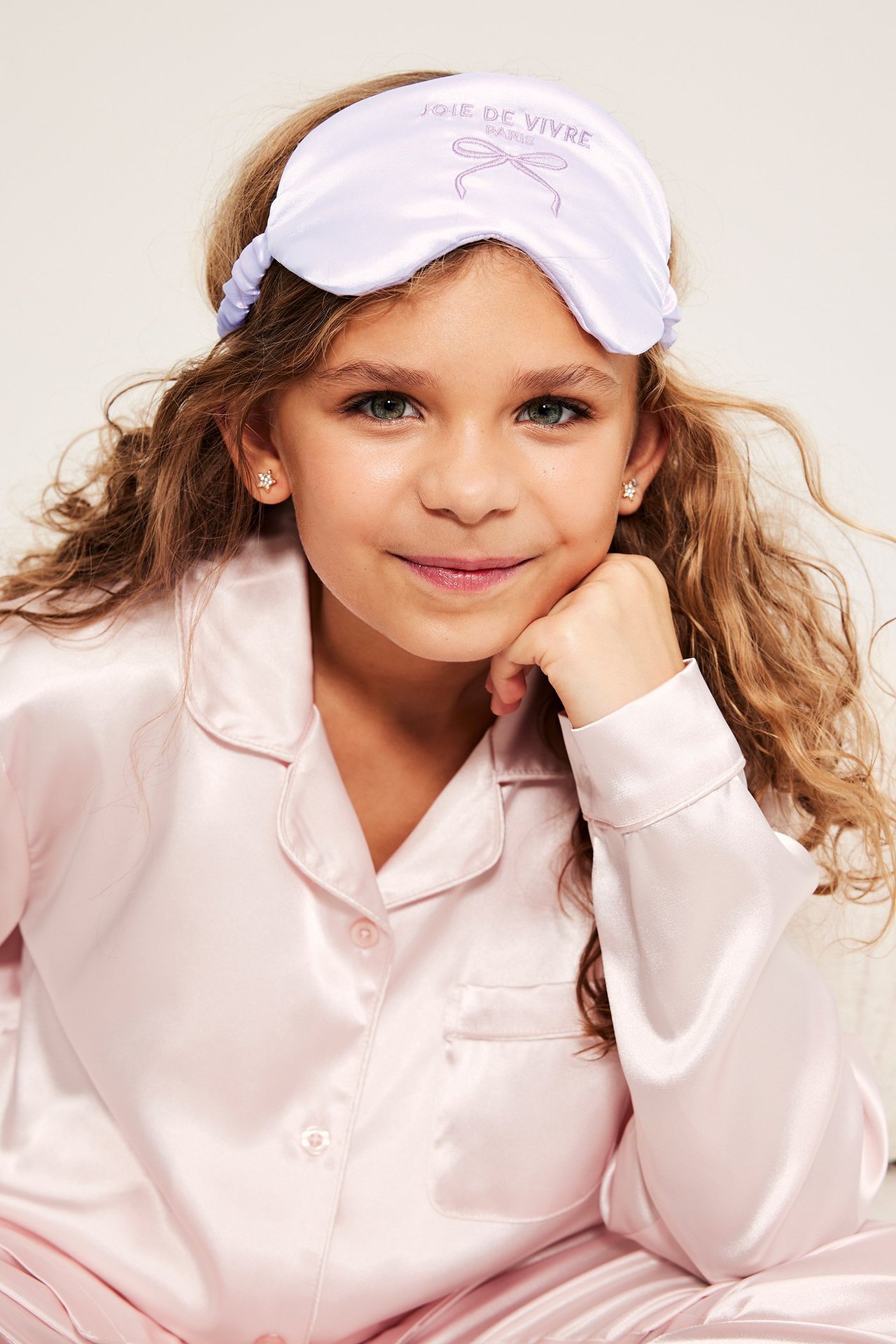 Nærbilde av et barn i lys lilla sateng sovemaske med broderi og lys rosa satengpyjamas.