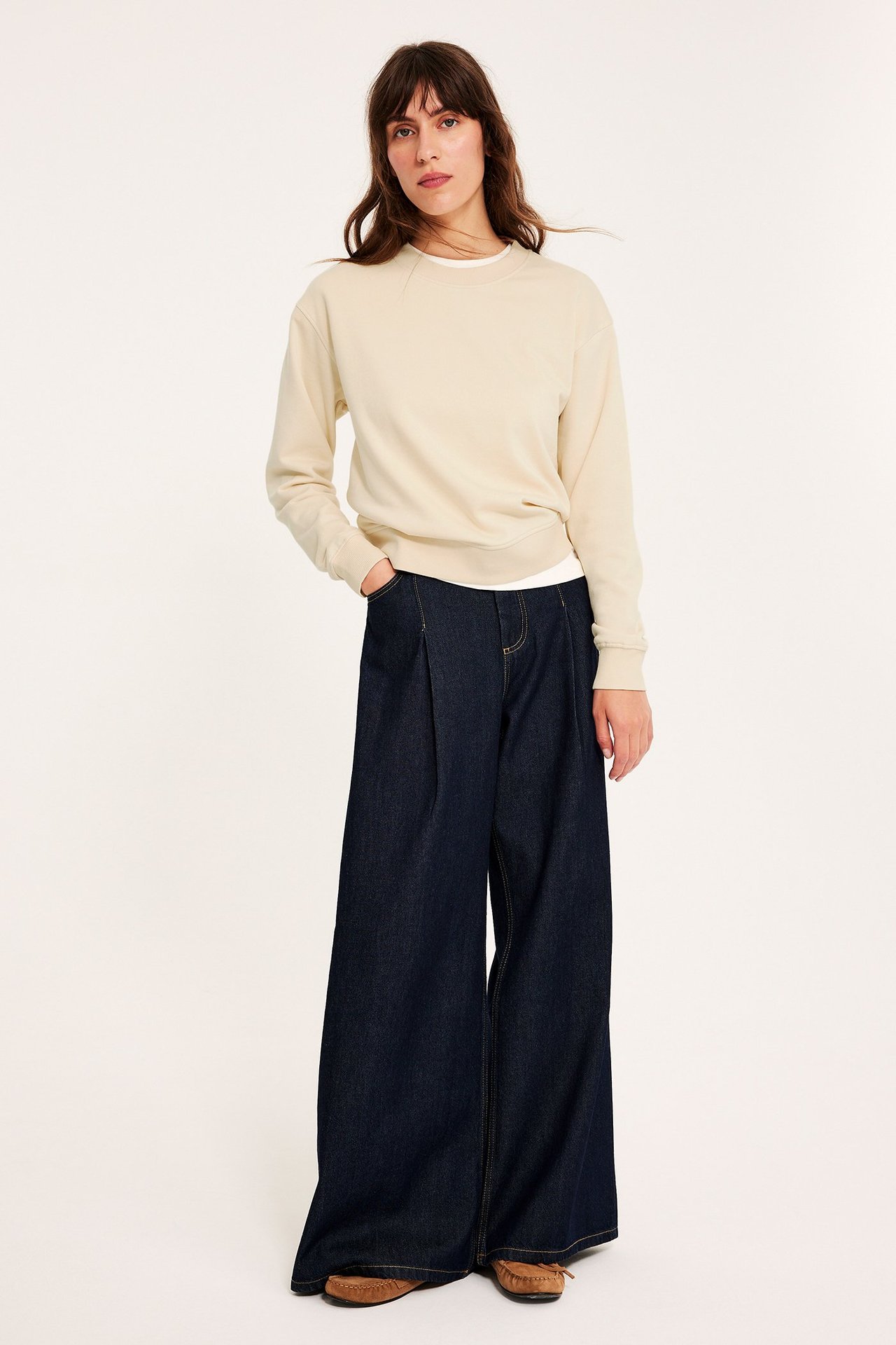 Edestä: Nainen luonnonvalkoisessa collegepaidassa, tummansinisissä leveälahkeisissa farkuissa ja ruskeissa mokkasiineissa.