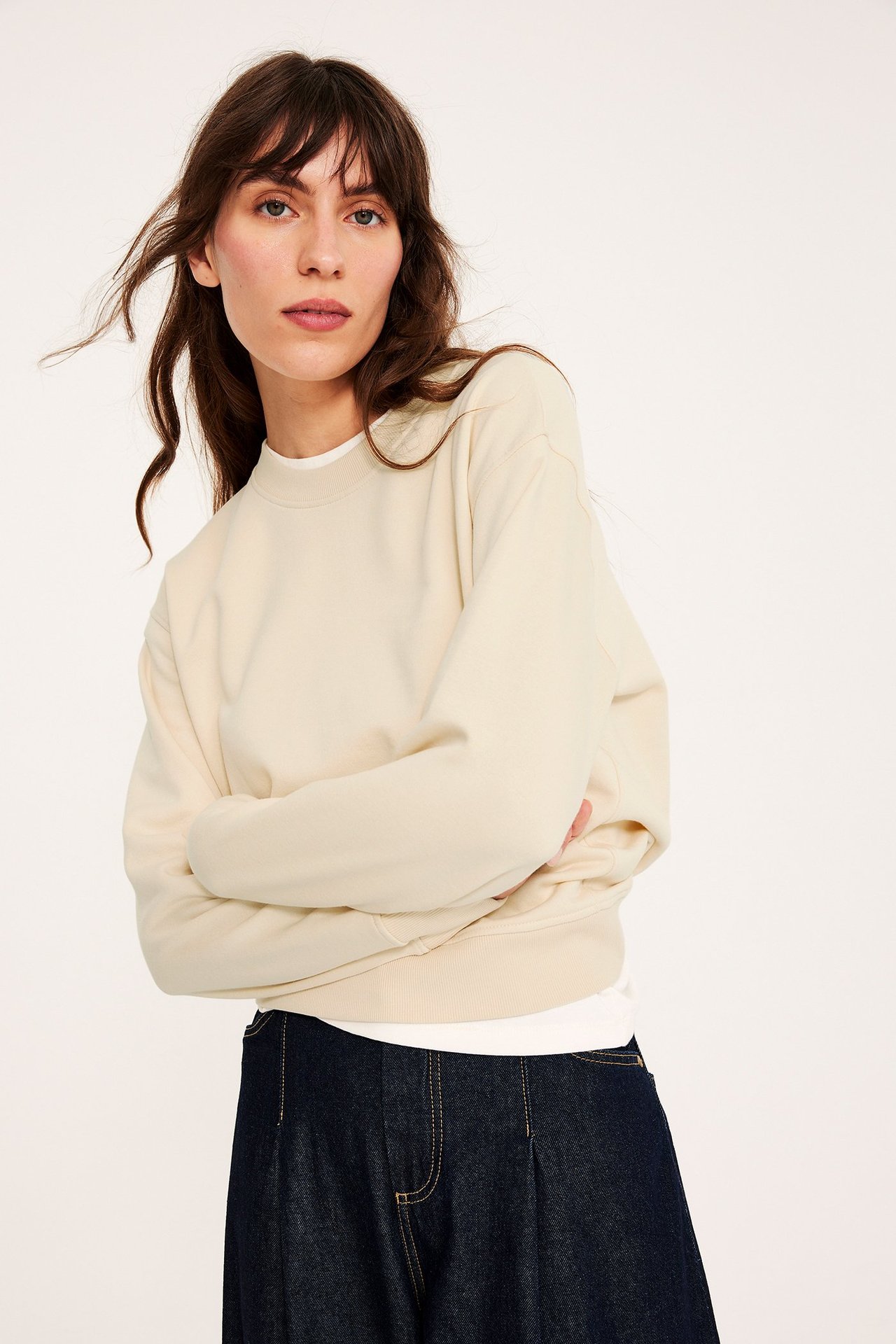 Edestäpäin: Nainen luonnonvalkoisessa pyöreäkauluksisessa collegepaidassa, valkoisen t-paidan ja tummansinisten farkkujen kanssa.