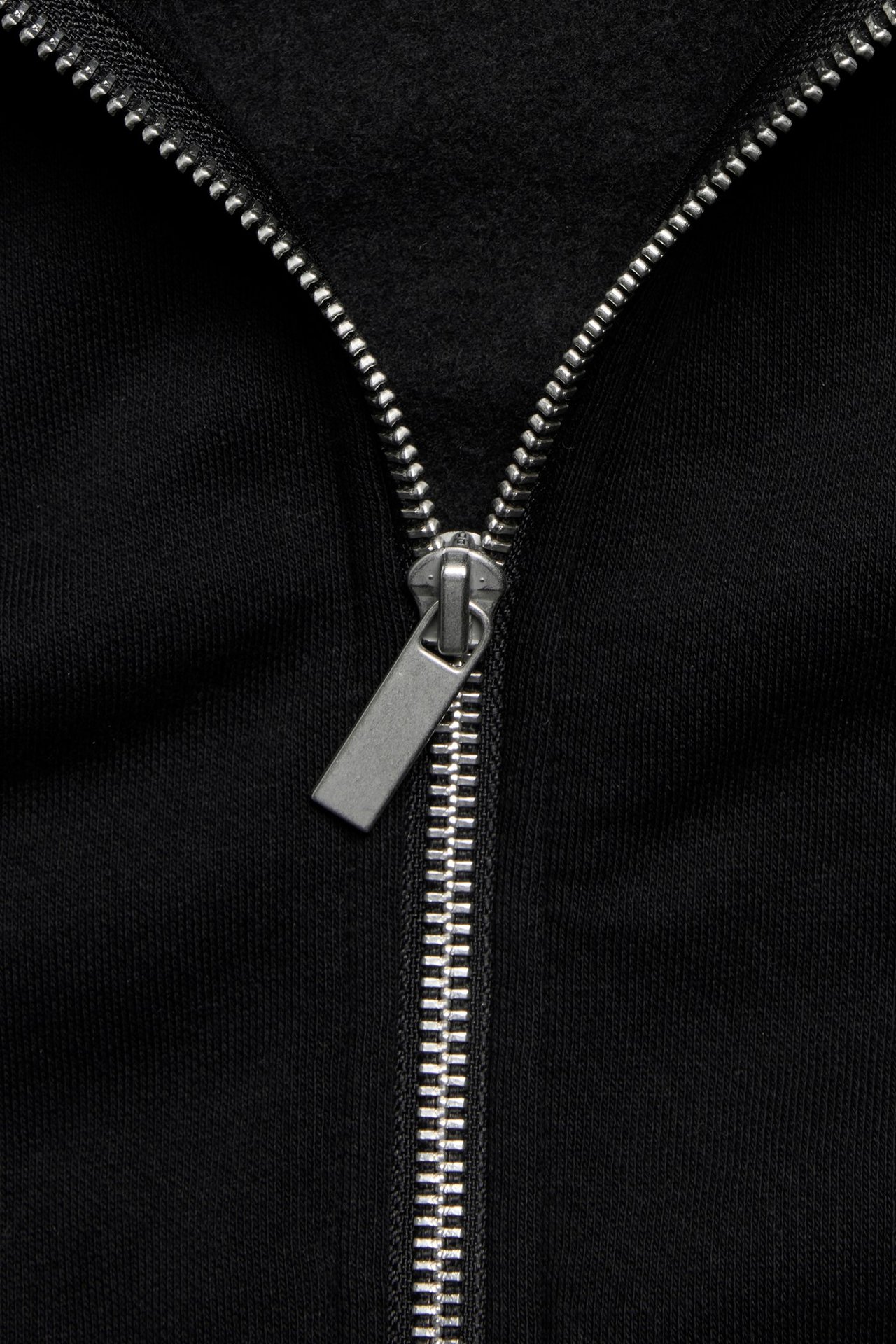 Zbliżenie na czarną bluzę z kapturem zapinaną na srebrny zamek błyskawiczny.