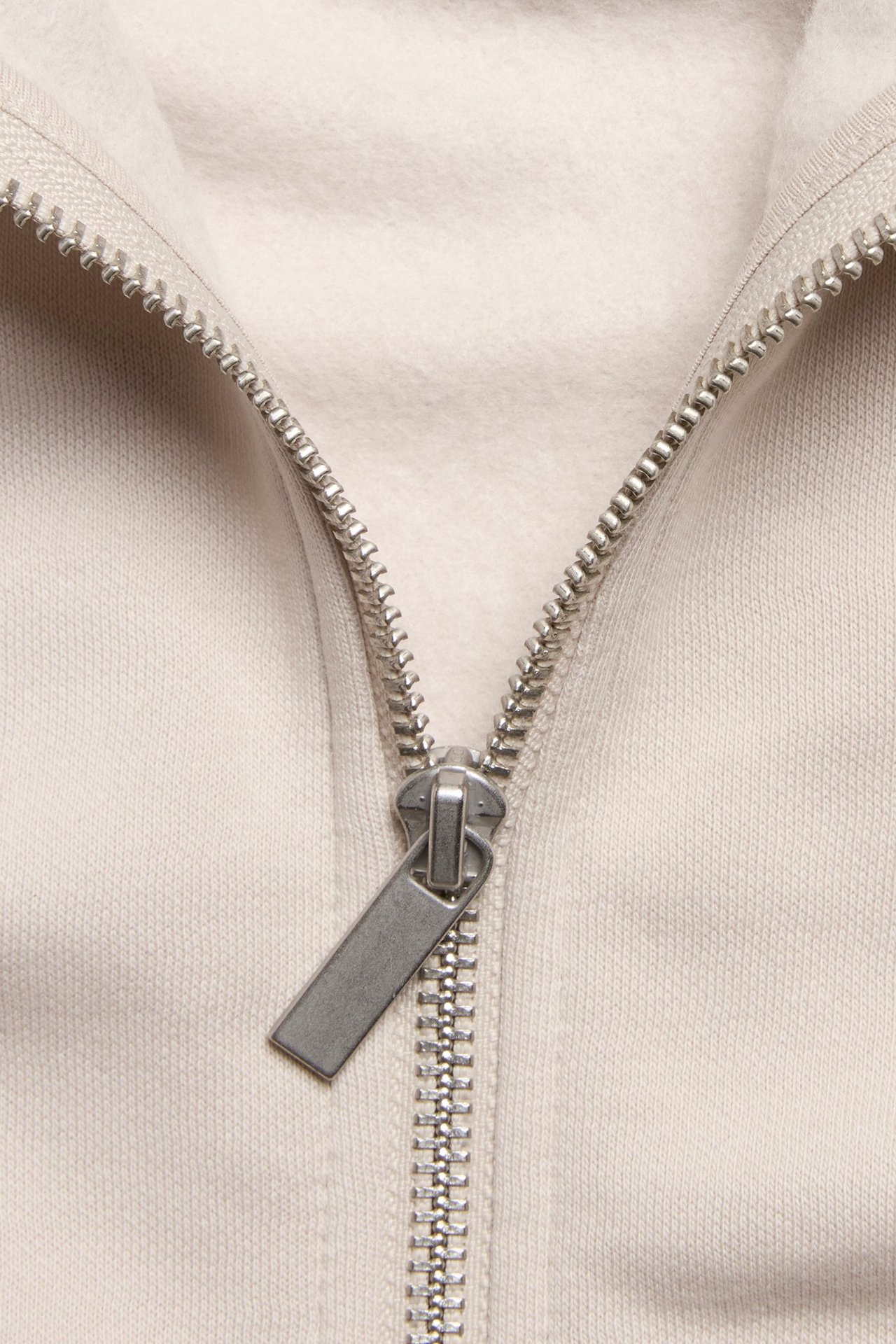 Zbliżenie beżowej bluzy z kapturem z mieszanki bawełny, z srebrnym zamkiem błyskawicznym.
