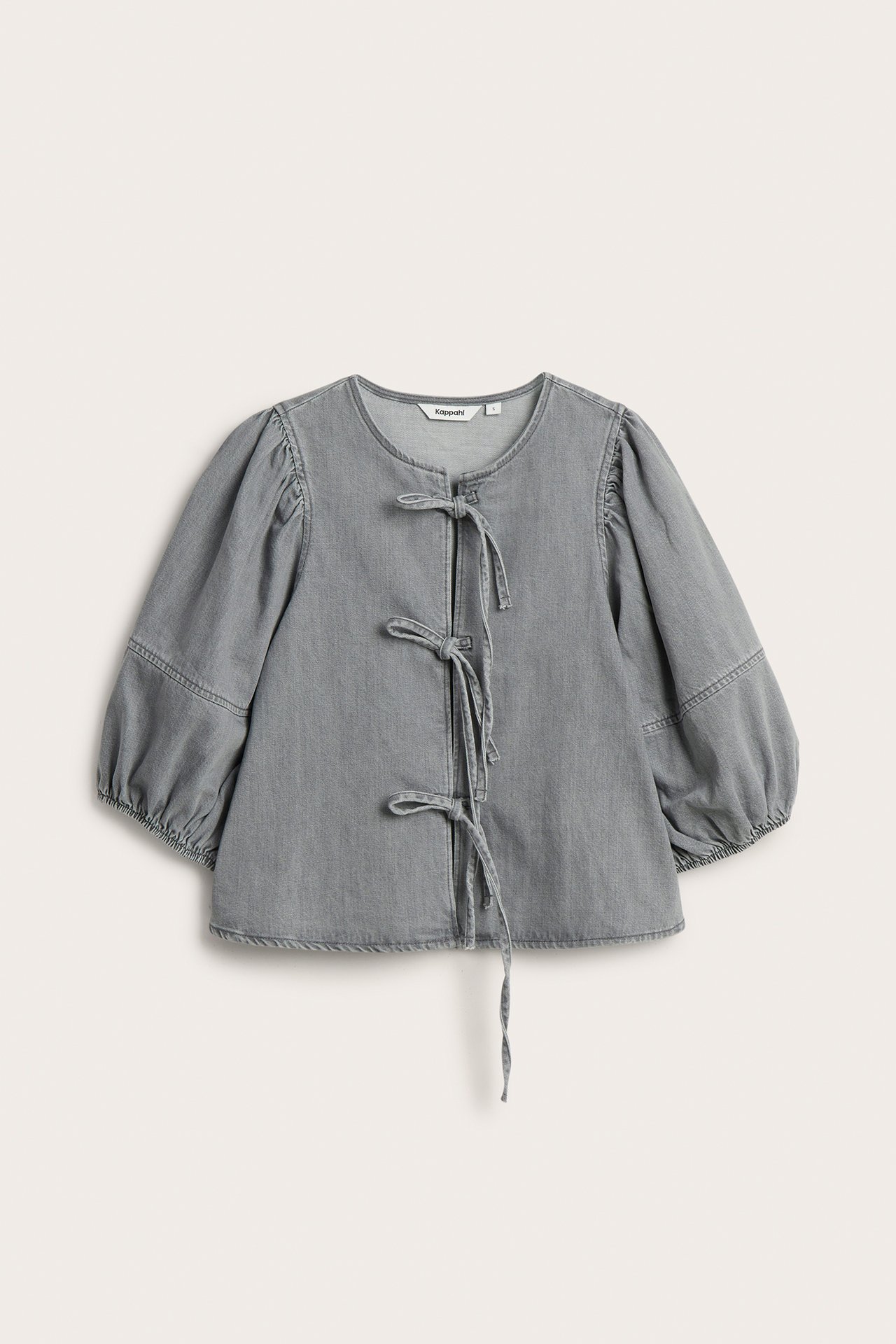 Framsida av en ljusgrå denimblus med rund hals, puffärmar och tre knytband fram.