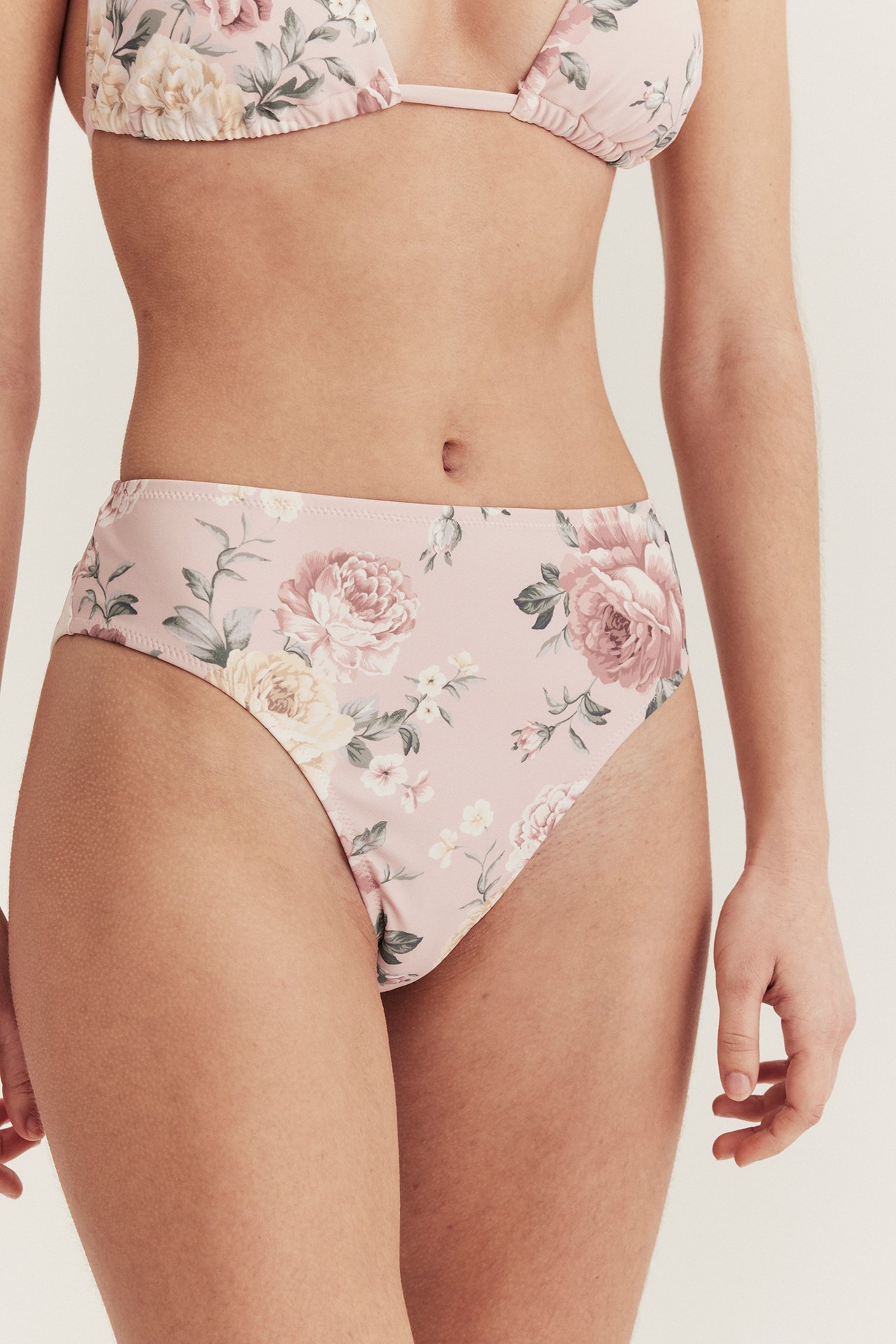 Frontvy av kvinna i rosa blommig högmidjad bikinitrosa och matchande bikinitopp.