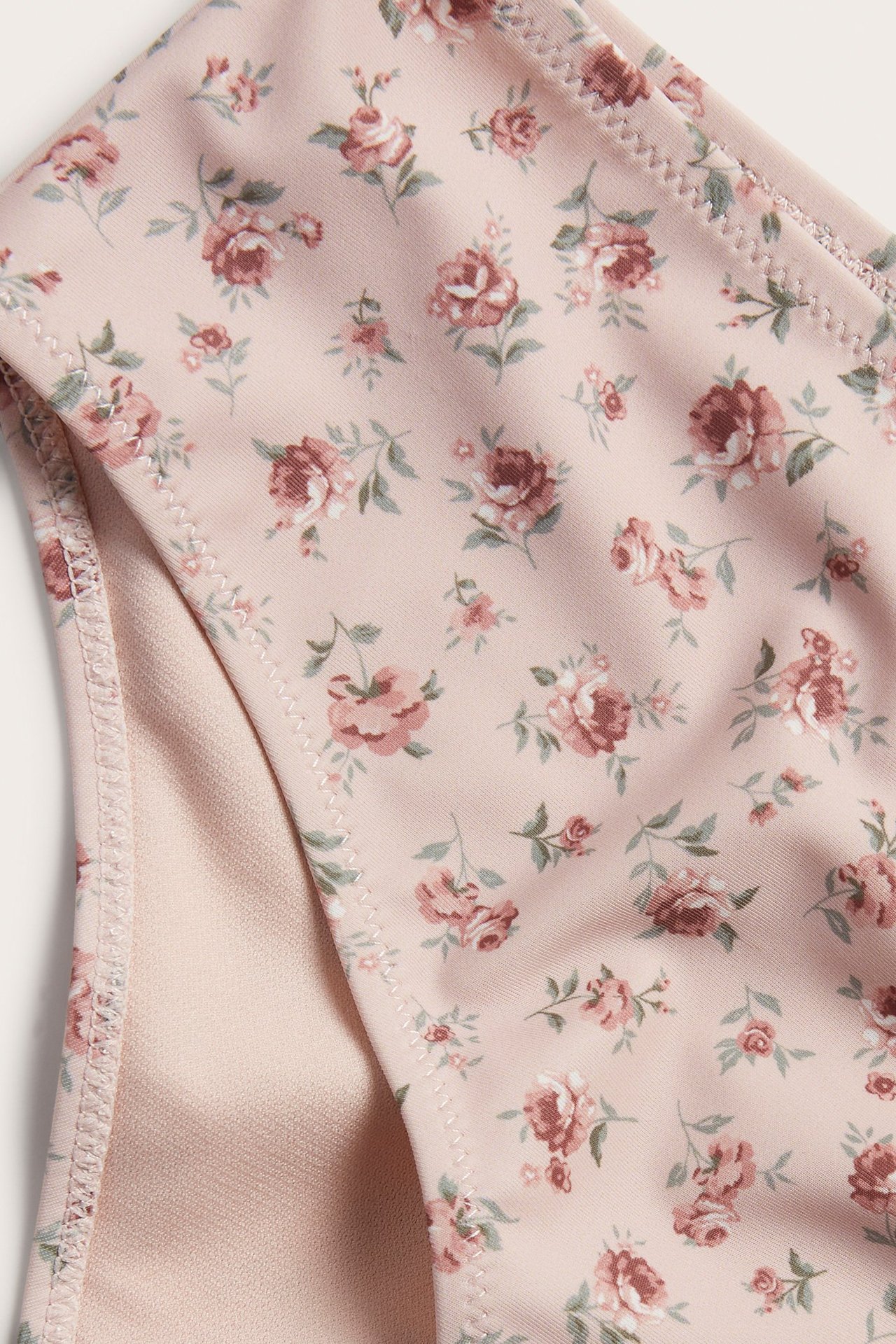 Zbliżenie różowych, kwiecistych majtek kąpielowych z wysokim stanem, ukazujące materiał i podszewkę.