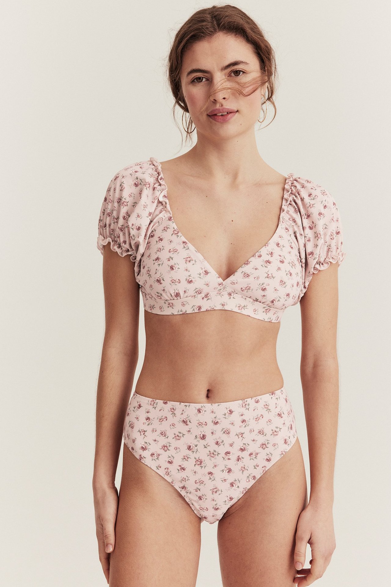 Widok z przodu kobiety w różowych, kwiecistych figach bikini z wysokim stanem i pasującym topie z falbankami.