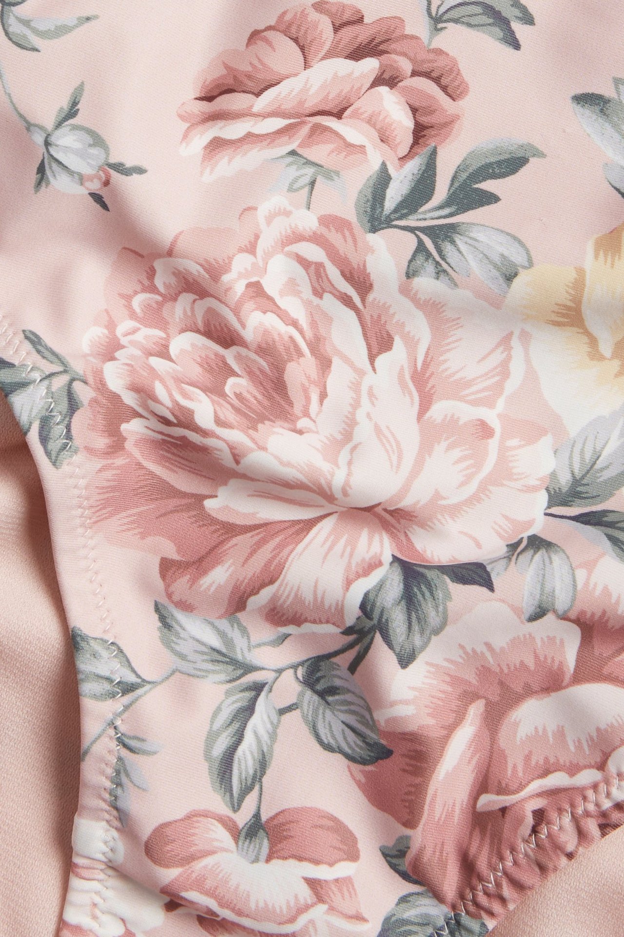 Zbliżenie różowego materiału od dołu bikini w kwiaty, z dużymi jasnoróżowymi i żółtymi kwiatami z zielonymi liśćmi.