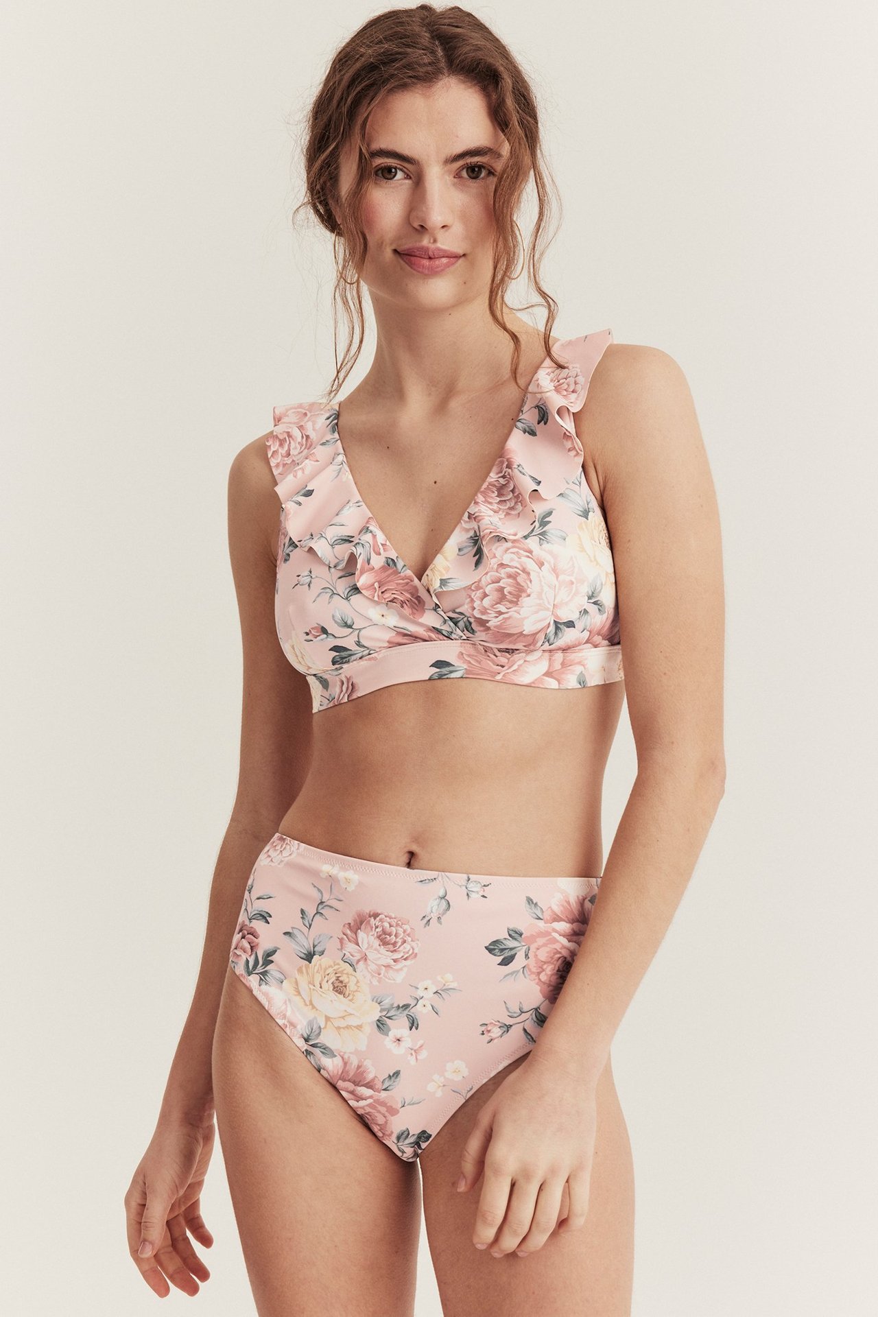 Kobieta w różowych, kwiecistych figach bikini z wysokim stanem i pasującym biustonoszu z falbankami.