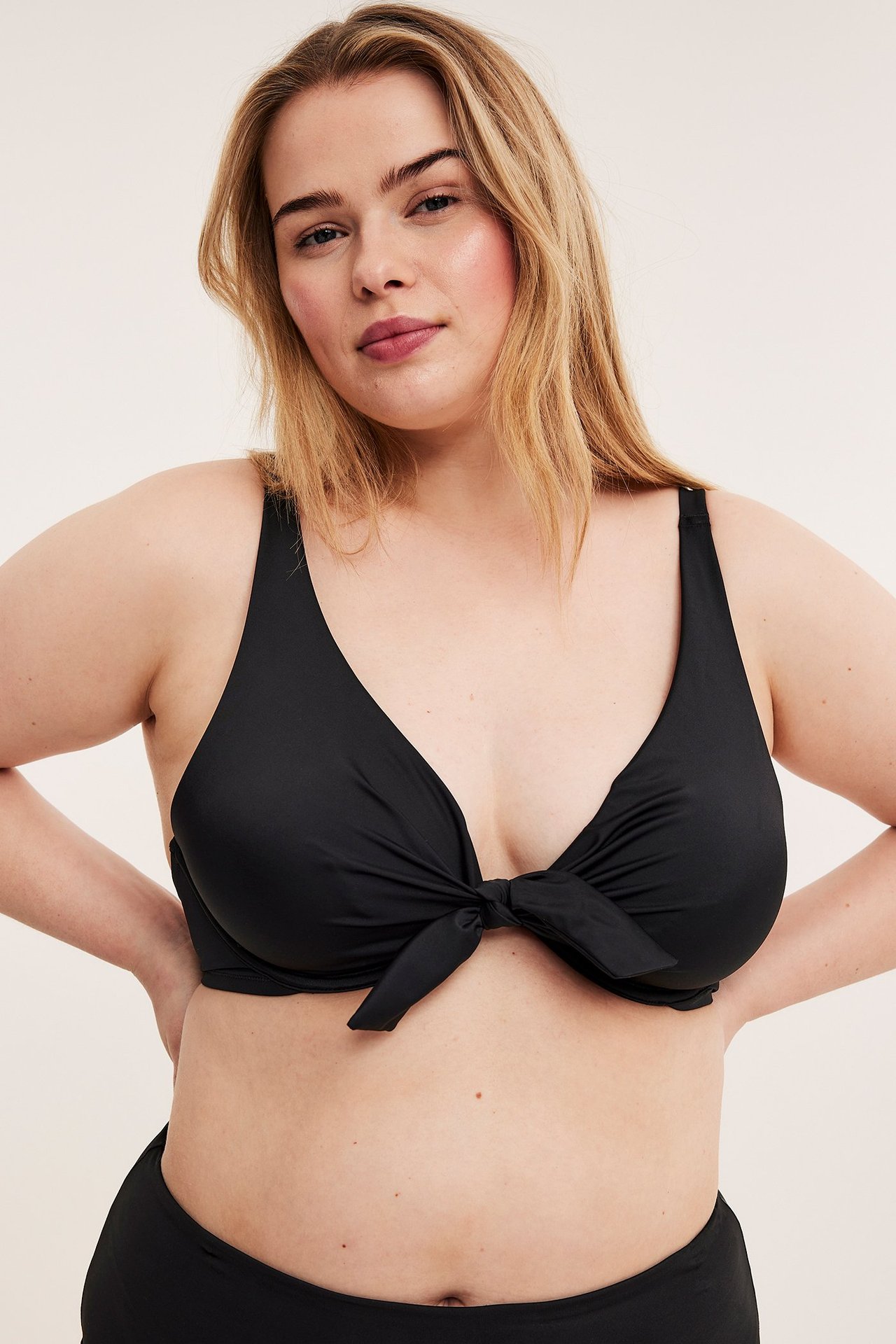 Widok z przodu kobiety w czarnym, nieusztywnianym biustonoszu bikini z fiszbinami i wiązaniem, oraz czarnych majtkach.