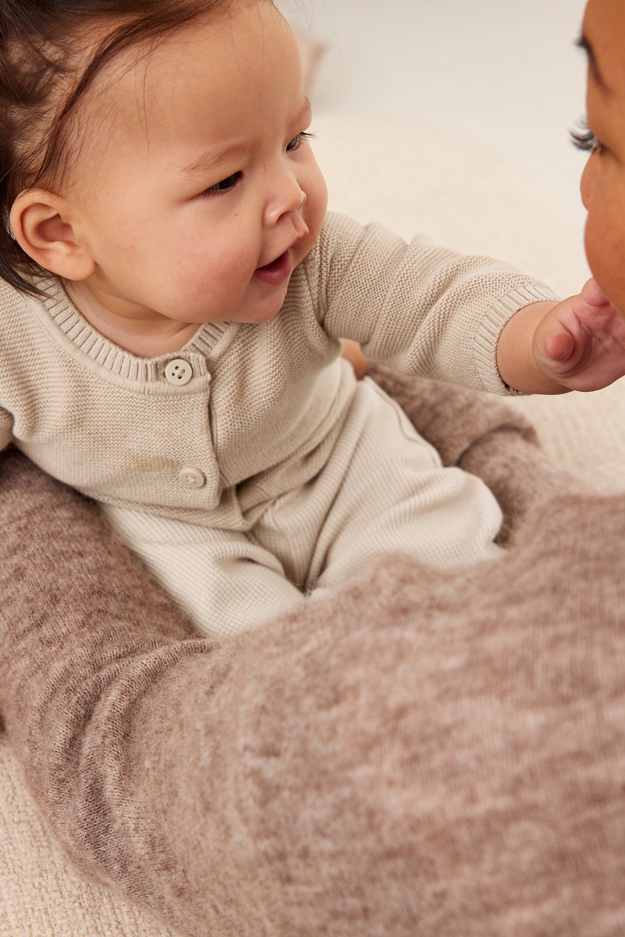 Närbild på baby i beige stickad kofta med knappar och ljusbeige byxor.