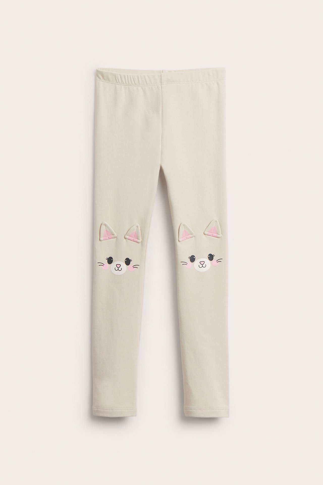 Frontvy av beiga mjuka leggings för barn med kattansiktsapplikationer och öron på knäna.