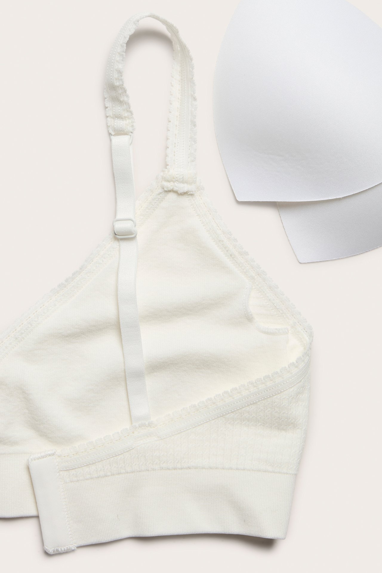Nærbilde av en offwhite sømløs strukturert BH med dekorerte justerbare stropper, hektefeste og polstring.