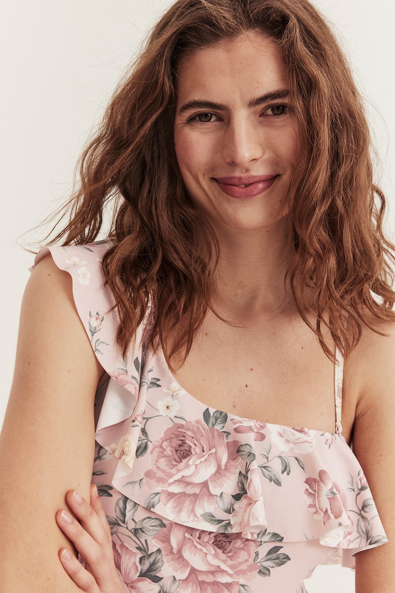 Närbild framifrån på en kvinna i rosa blommig baddräkt med asymmetrisk volanghalsringning.