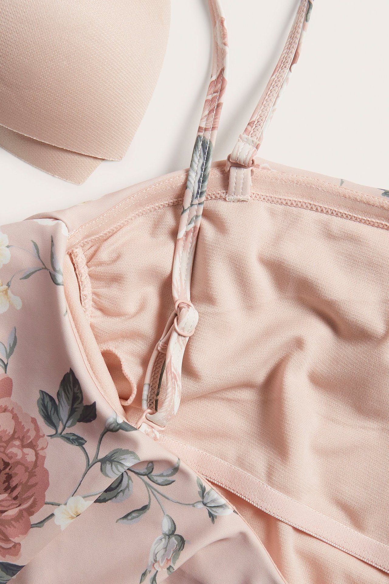 Zbliżenie różowego kwiecistego kostiumu kąpielowego z regulowanym ramiączkiem, gładką podszewką i wyjmowaną wkładką biustonosza.
