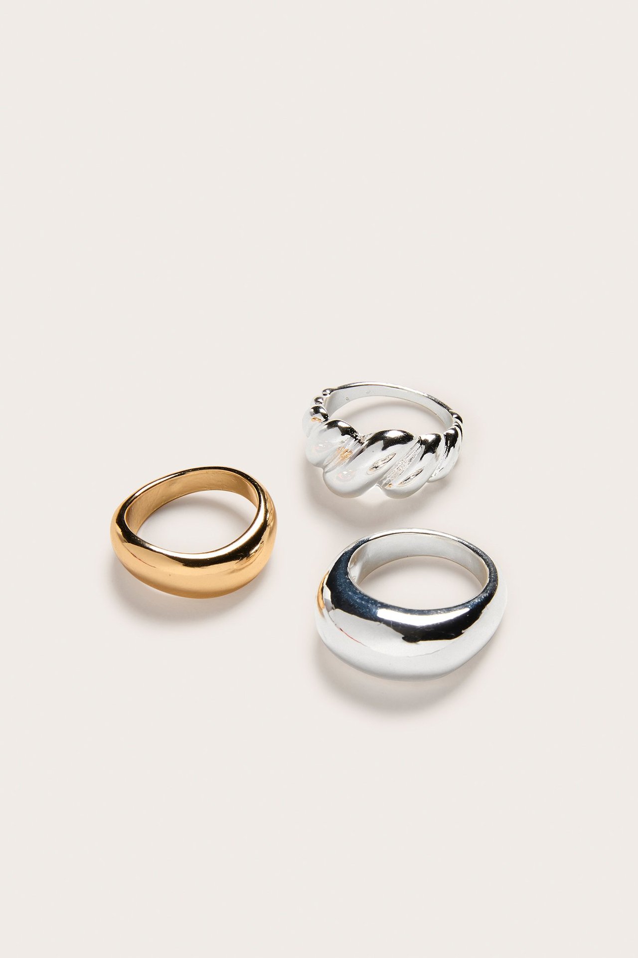Närbild av ett 3-pack ringar: en guld, en silver tvinnad och en silver kupolformad ring.