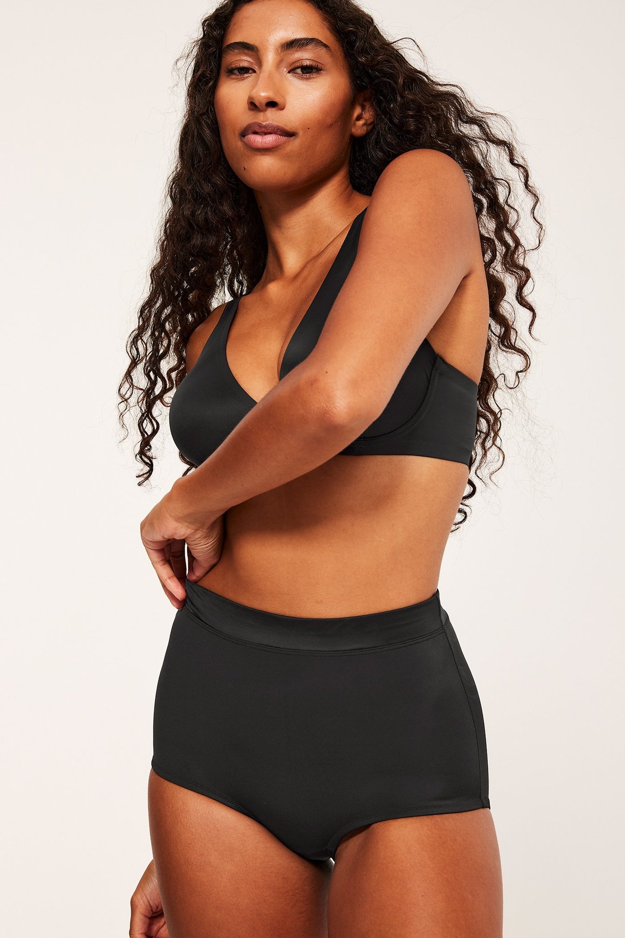 Forfra: kvinne i svarte høytlivs shaping hipster-truser og matchende svart V-hals BH.