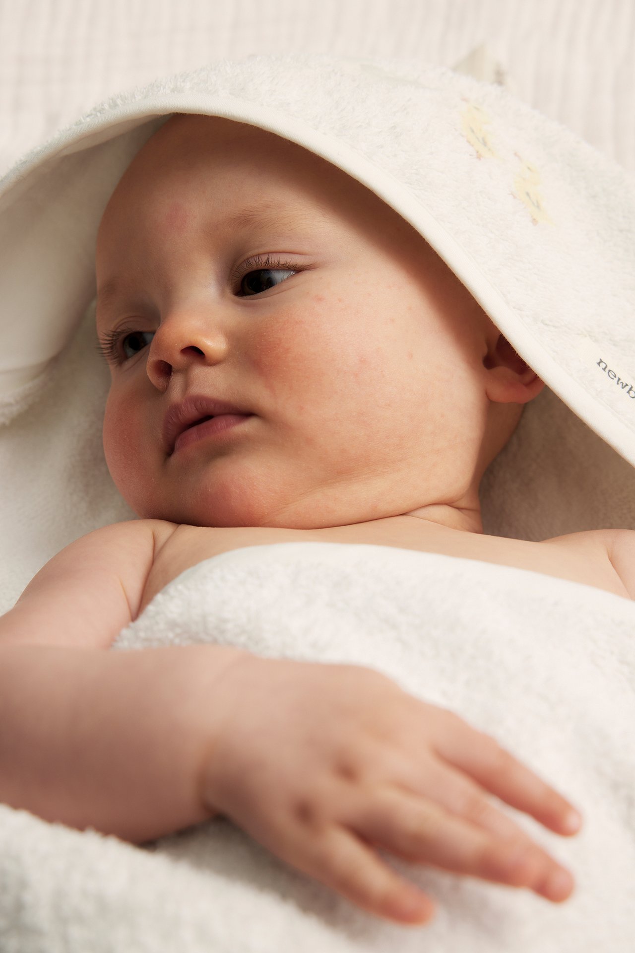 Närbild på baby inlindad i en naturvit huvhandduk i frotté med diskret brodyr.