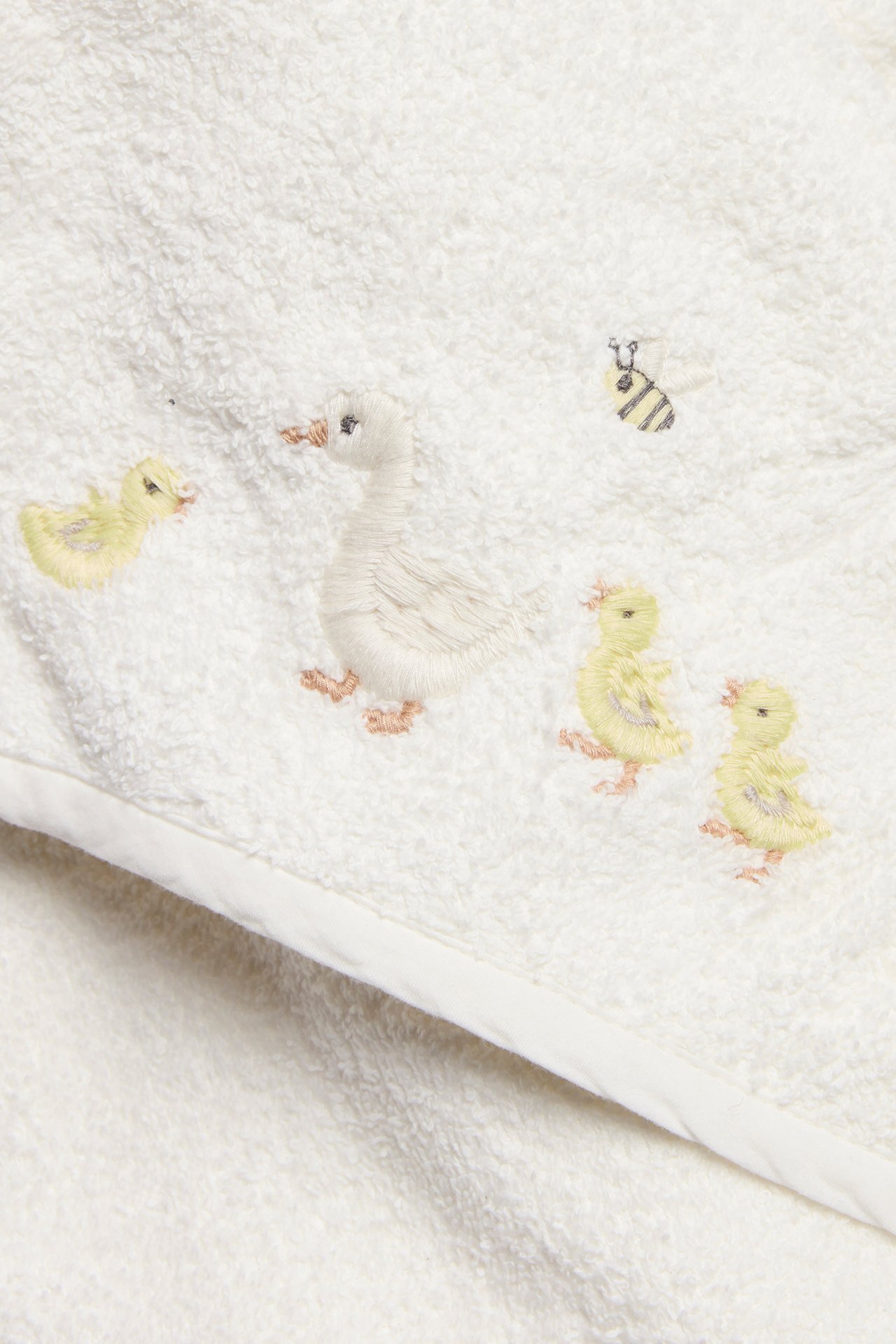 Närbild av en offwhite frottéhandduk med huva för baby, med broderade anka, ankungar och bi.