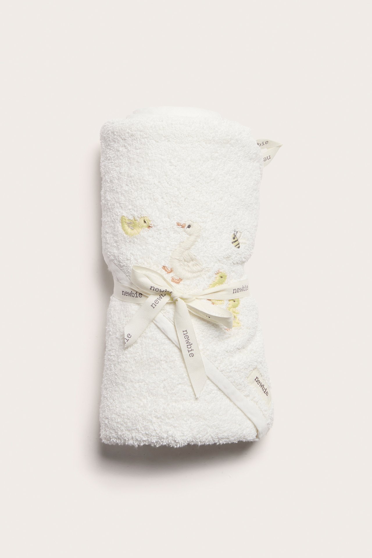 Framifrån: Offwhite frottéhandduk med huva för baby, med anka- och bibroderi, knuten med band.