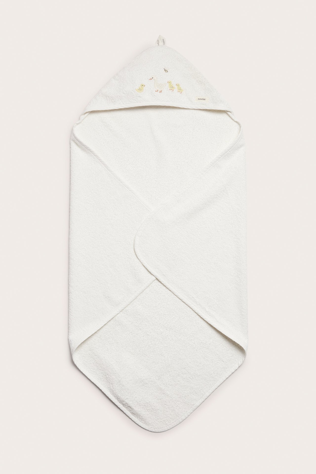 Framifrån, en offwhite frottéhandduk med huva för baby, med broderi av ankor på huvan.