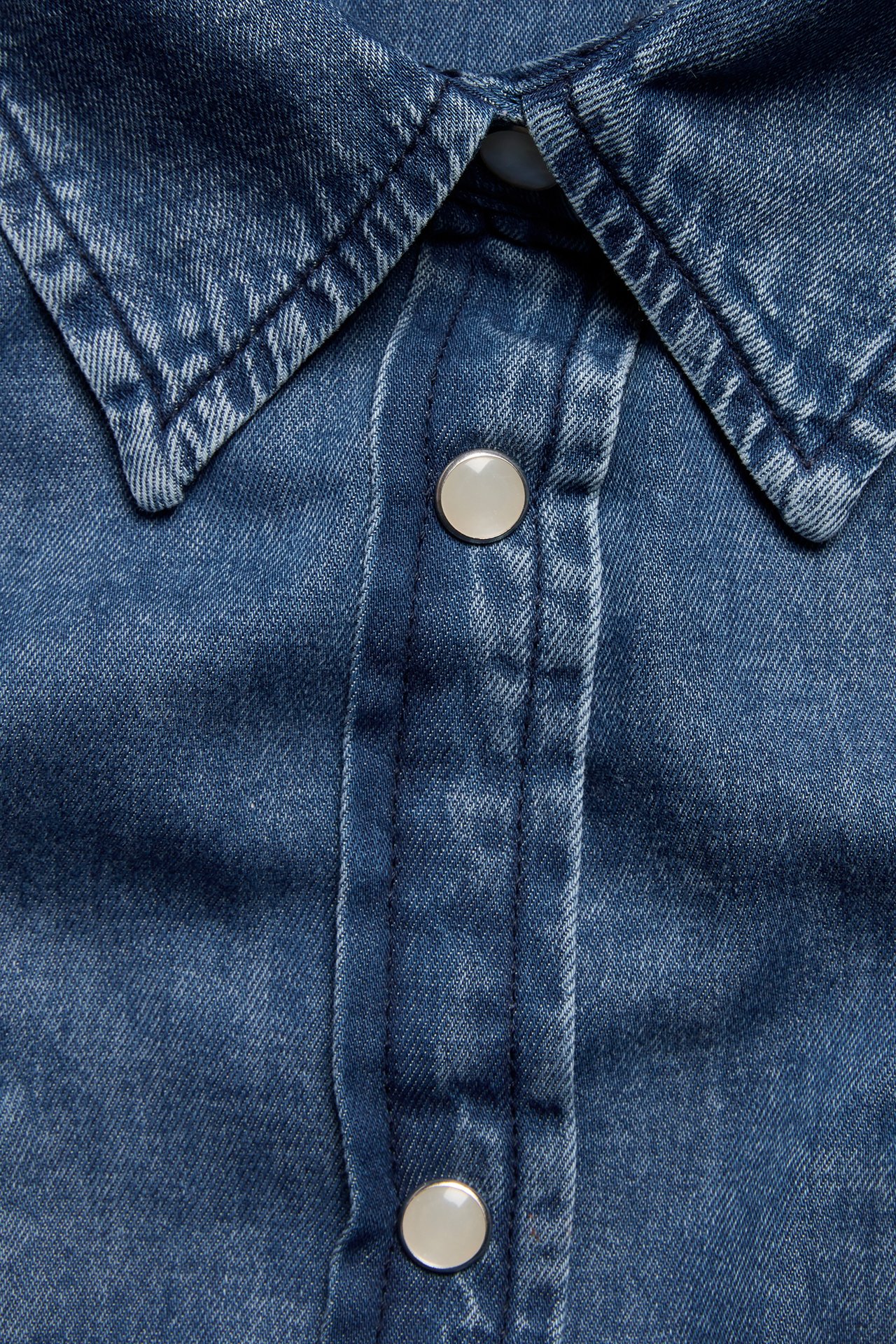 Lähikuva tummasta denimpaidasta, jossa on kaulus ja hopeiset painonapit etulistassa.