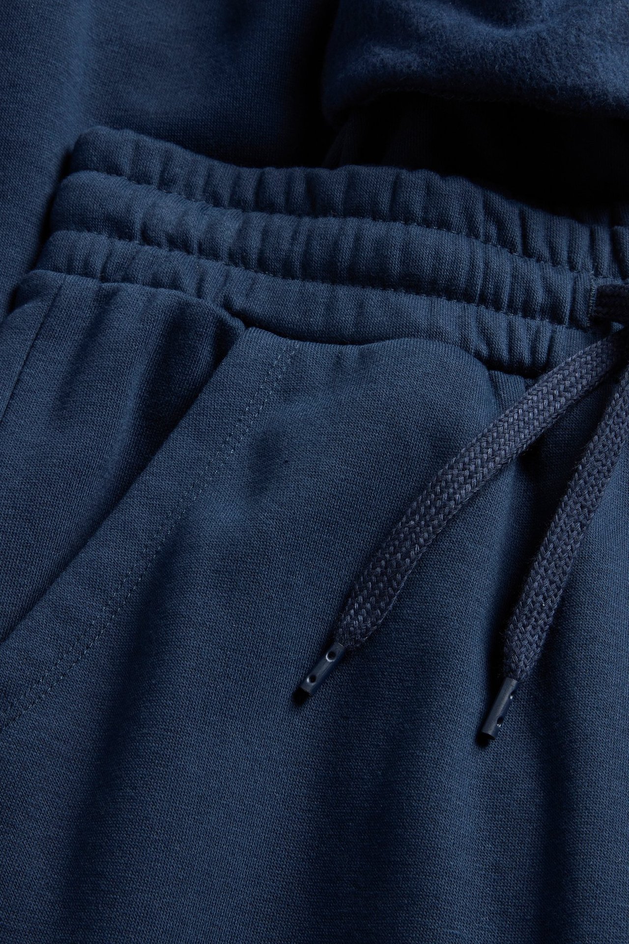 Zbliżenie na ciemnoniebieskie spodnie dresowe z elastycznym pasem, sznurkiem i boczną kieszenią.