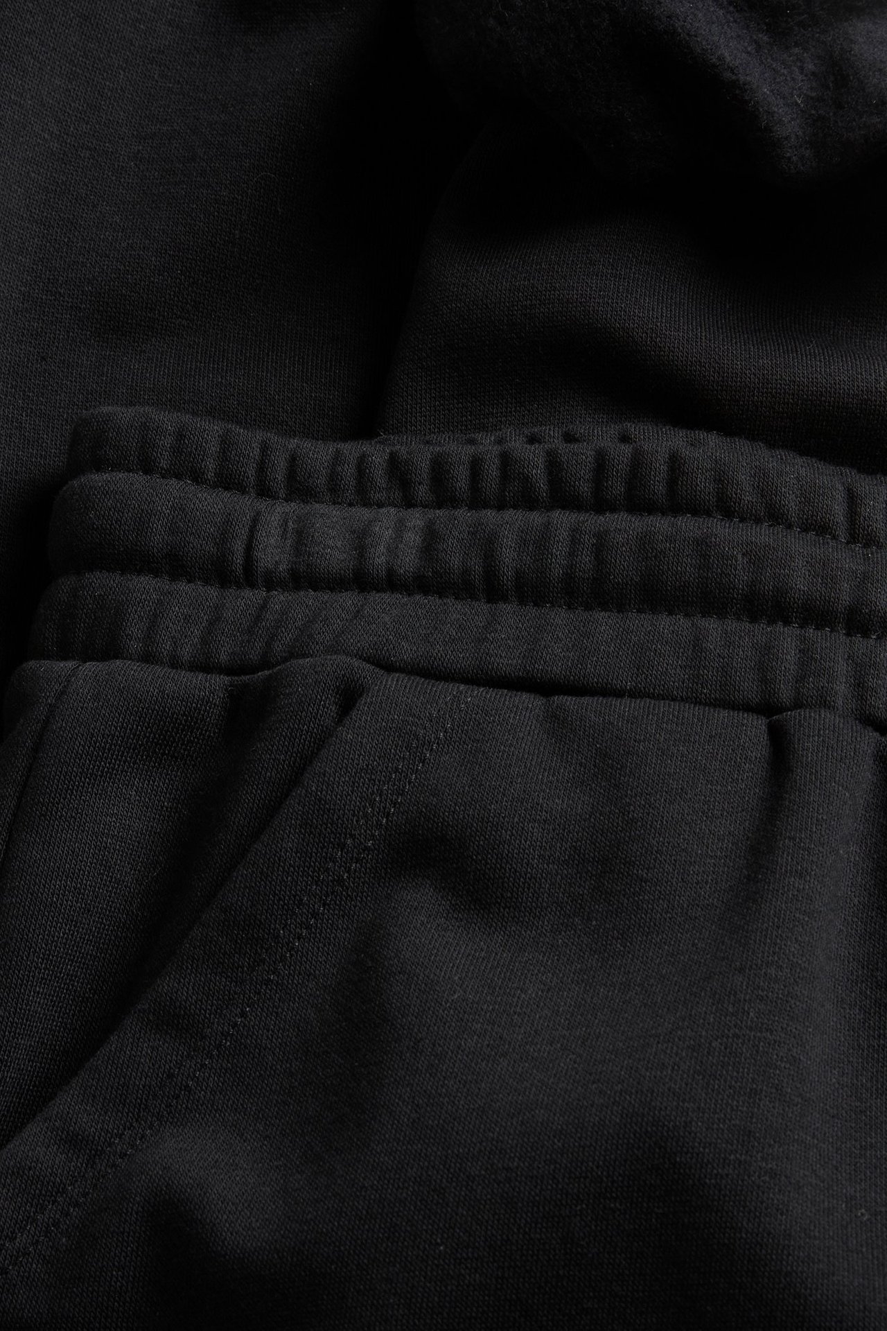 Zbliżenie na czarne spodnie dresowe z mieszanki bawełny z elastycznym pasem i boczną kieszenią.