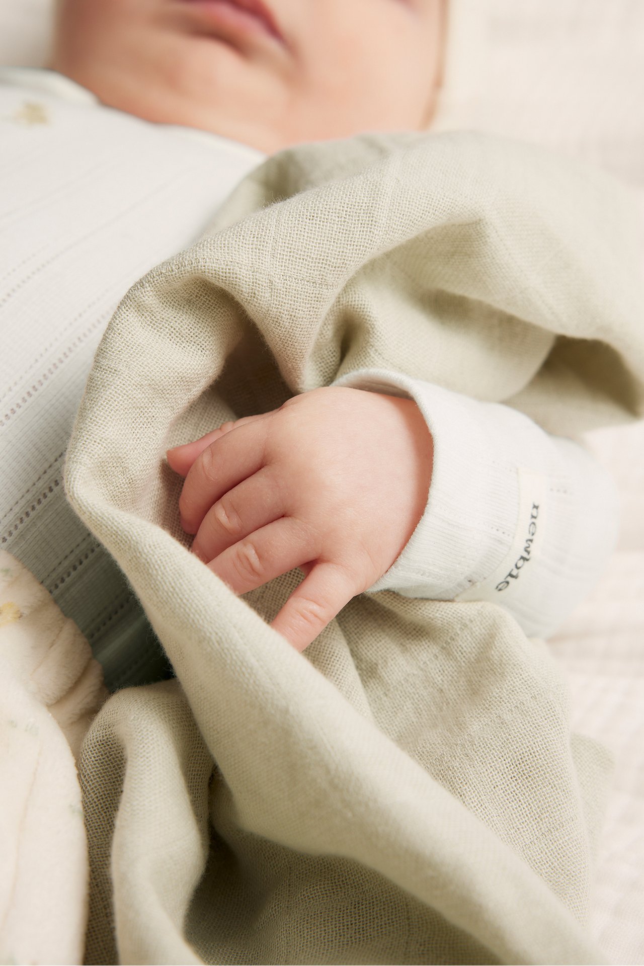 Zbliżenie na dziecko w kremowym, długim body z prążkowanej dzianiny, z ręką na jasnozielonym kocyku.