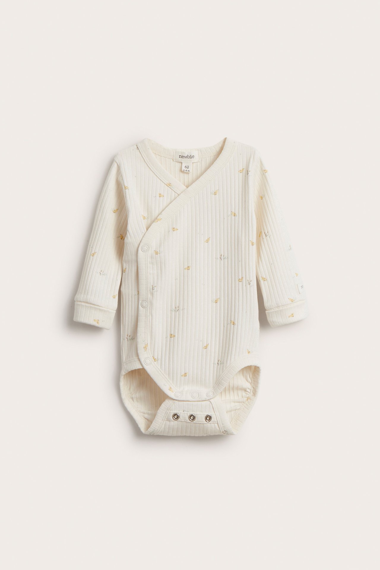 Frontvisning av en offwhite ribbet bomulls omslagsbody for baby med diskret mønster og trykknapper.
