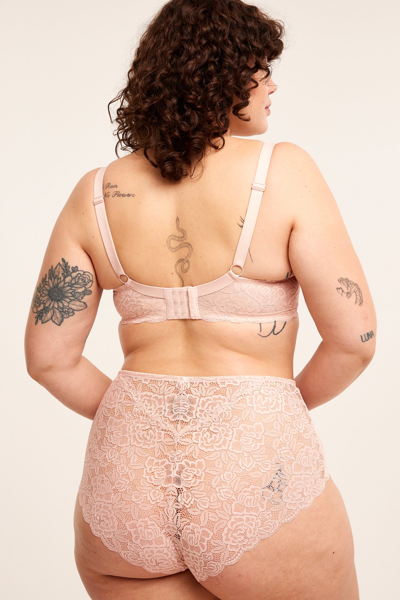 Bakfra av en kvinne i rosa høytlivs brazilian-truse i blonde og en matchende blonde-BH.