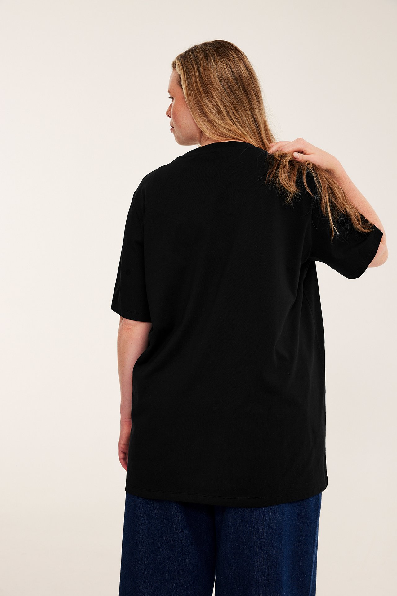 Bakfra av kvinnelig modell i svart oversized t-skjorte og mørkeblå vide jeans.